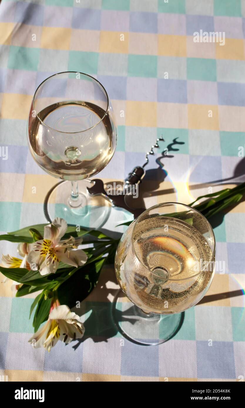 Bicchieri da vino con vino bianco, fiori e cavatappi dall'alto su una tovaglia a scacchi con spazio per la copia Foto Stock