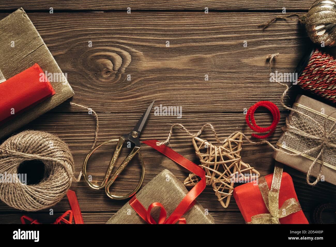 Confezione regalo di Natale, preparazione per la festa. Regali avvolti, nastri, forbici e carta su sfondo di legno. Vista dall'alto. Spazio per il testo. Foto Stock