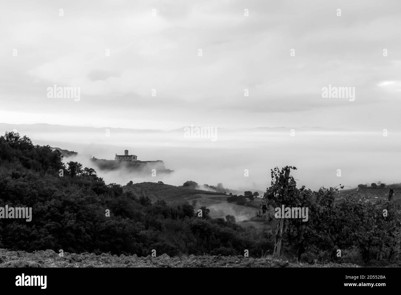 Vista surreale di una piccola cittadina umbra quasi completamente nascosta dalla nebbia con silhouette di alberi in primo piano Foto Stock