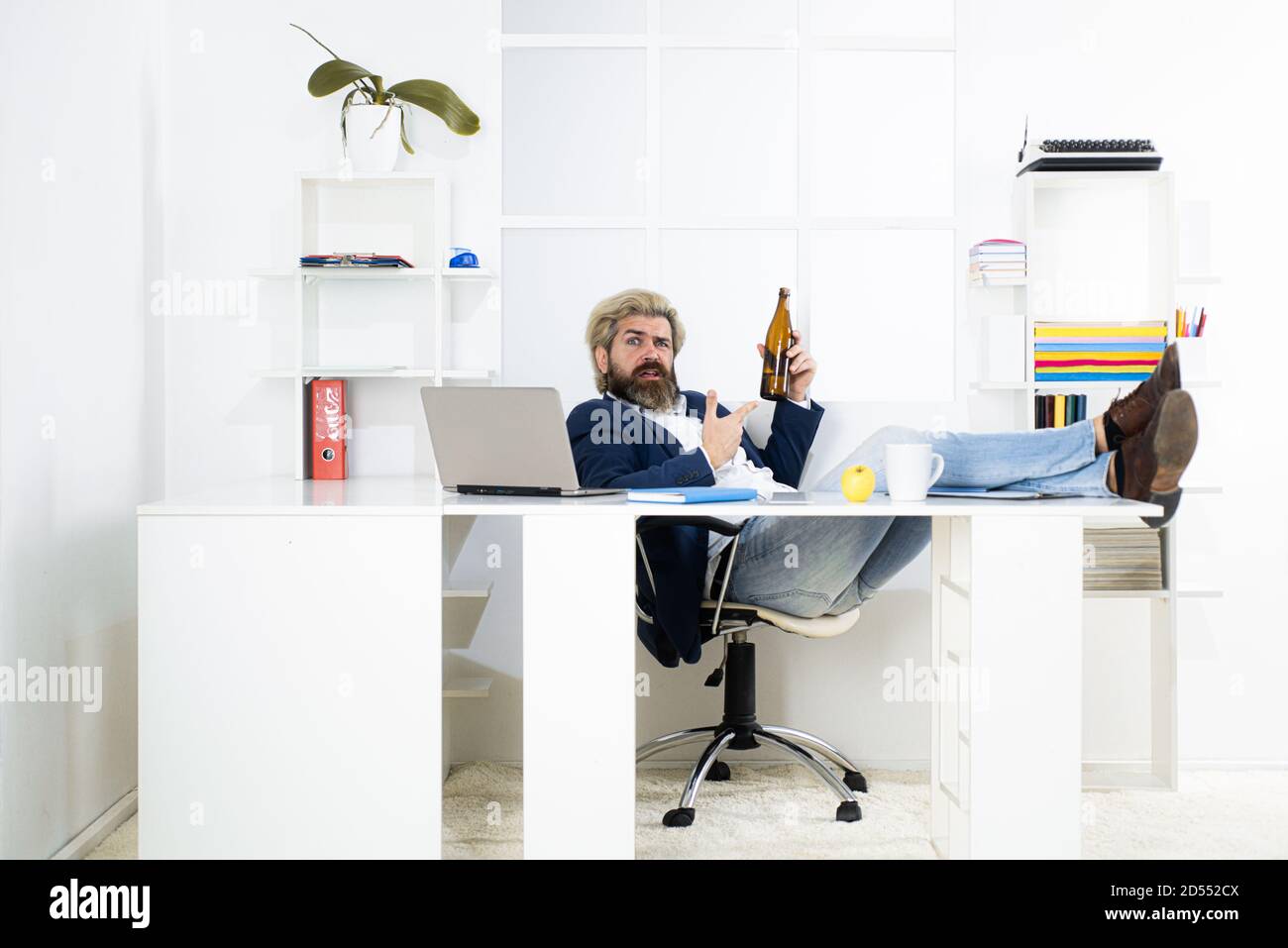 Uomo d'affari stanco annoiato che brilica sul posto di lavoro vicino al laptop, lavoro noioso, lavoro di fine lavoro morto, overwork extra dopo l'orario di lavoro, bere alcol. Foto Stock