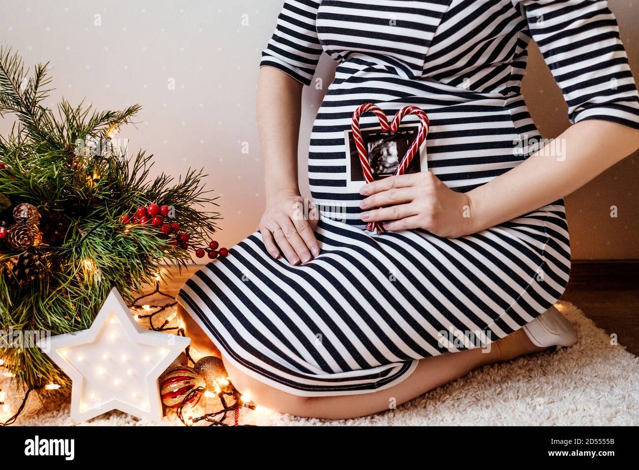 Primo piano di una donna incinta tagliata che fa un cuore da lollipop e ultrasuoni all'interno sul suo ventre. Decorazioni natalizie su sfondo. Foto Stock