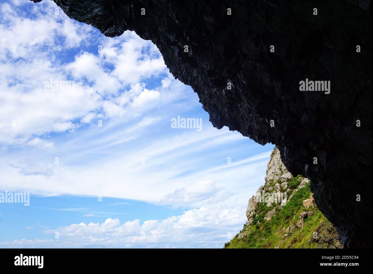 Una bella vista si apre attraverso il buco dalla grotta: Montagne, cielo blu chiaro e nuvole bianche. Parete scura sopra l'uscita. All'interno c'è oscurità, bu Foto Stock
