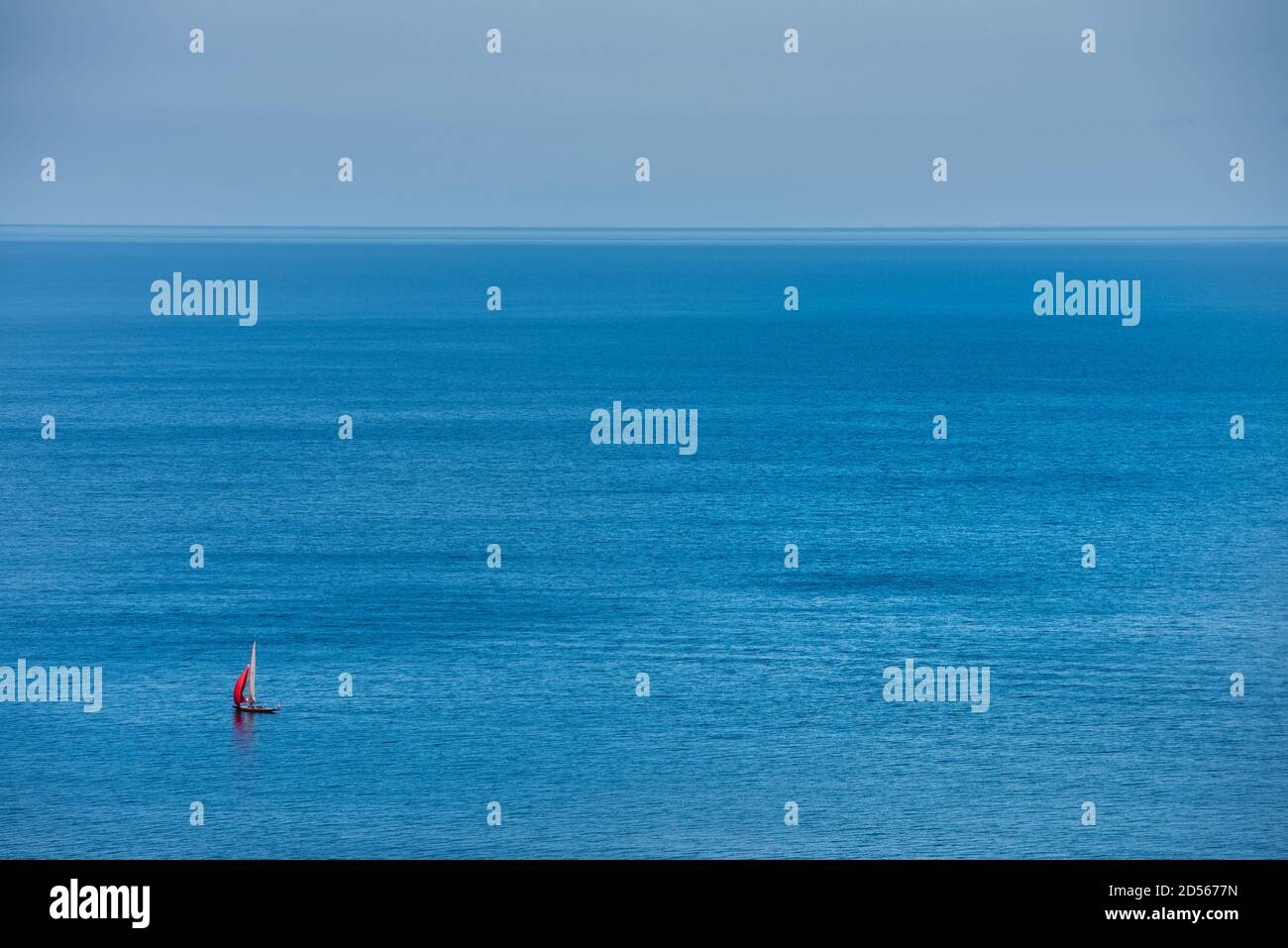 Una barca a vela solitaria che attraversa un oceano blu e tranquillo vicino a Mons Klint. L'equipage o il marinaio gode di una rilassante fuga nel Mar Baltico Foto Stock