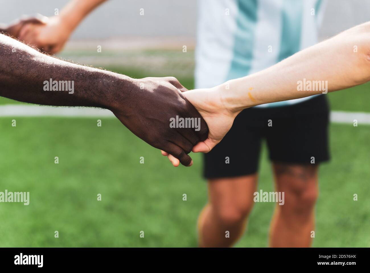 mani bianche e nere che si tengono insieme in un gruppo multietnico di giovani che giocano a calcio. squadra di persone che gioca a sport, simbolo del potere unificante a. Foto Stock