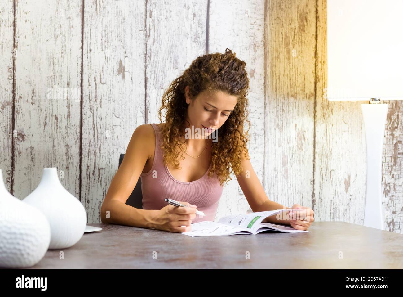 Attraente giovane donna che lavora su crossword puzzle a casa in una rivista seduta ad un tavolo con copyspace Foto Stock