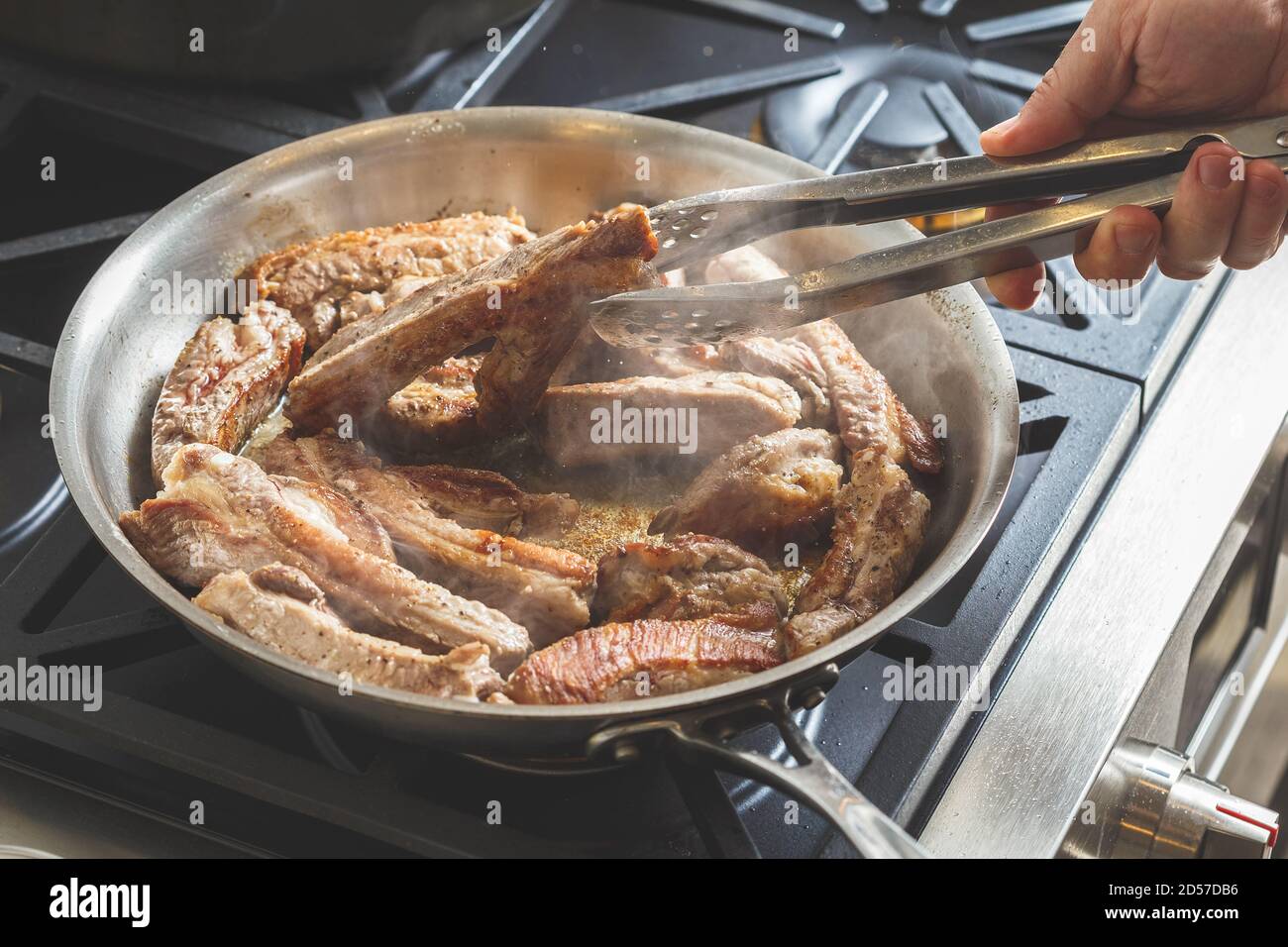 Mano dell'uomo arrostire le costolette di maiale su una teglia di acciaio. Preparazione della cena Foto Stock