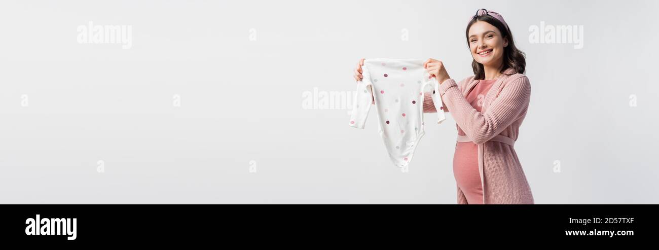 concetto orizzontale di gioiosa donna incinta nella fascia che tiene il bambino romper isolato su bianco Foto Stock