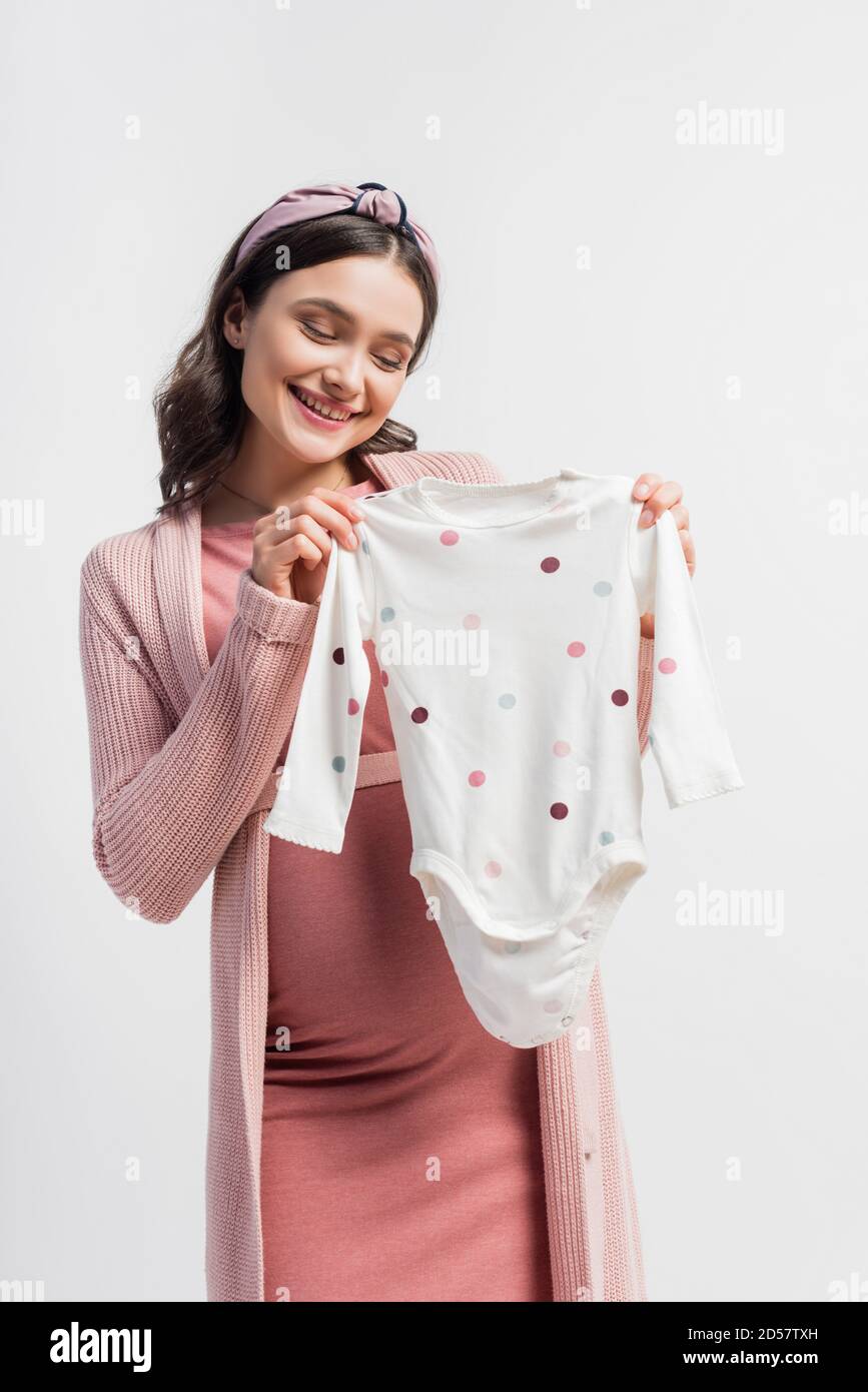 gioiosa donna incinta nel archetto che tiene il romper del bambino isolato sopra bianco Foto Stock