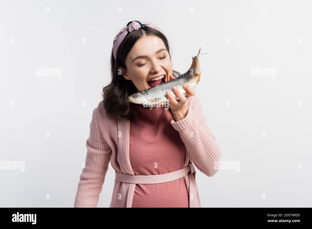 donna incinta con bocca aperta e occhi chiusi che tengono asciugato pesce isolato su bianco Foto Stock