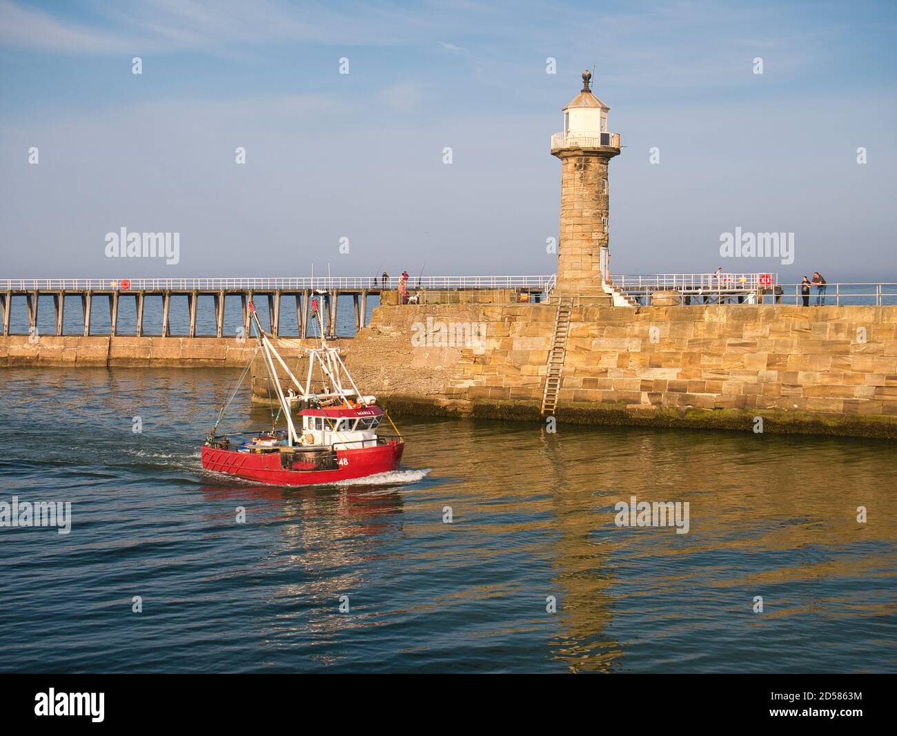Una barca da pesca rossa torna a Whitby Harbour sulla costa orientale del North Yorkshire, Inghilterra, Regno Unito - preso alla fine del pomeriggio Foto Stock