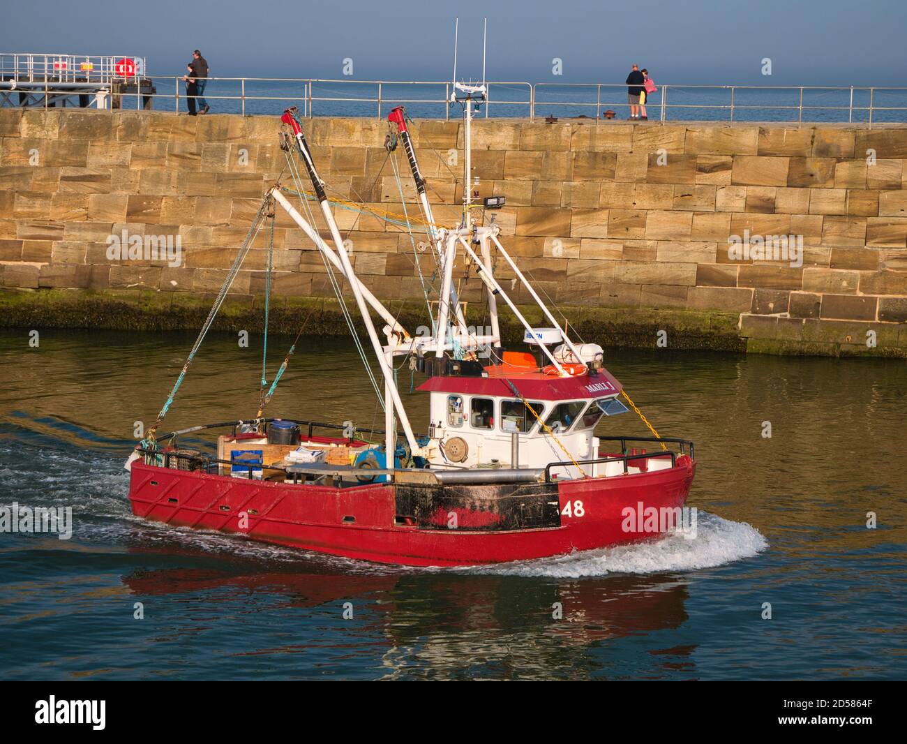 Una barca da pesca rossa torna a Whitby Harbour sulla costa orientale del North Yorkshire, Inghilterra, Regno Unito - preso alla fine del pomeriggio Foto Stock