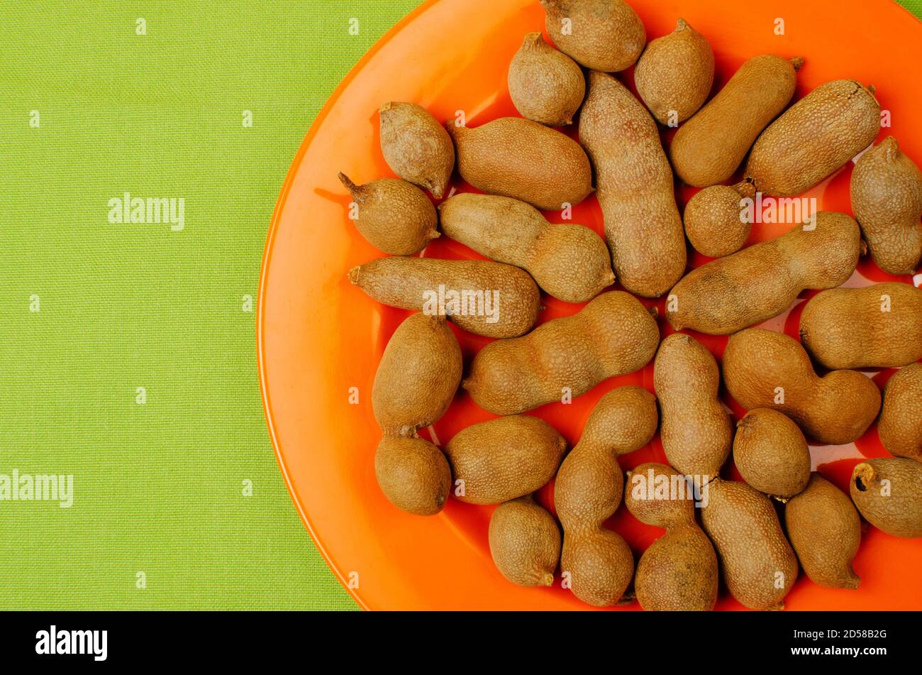 Tamarind, Tamarindus indica frutta a cialde. Contiene una polpa dolce e piccante. Posizionato su una piastra di colore arancione Foto Stock