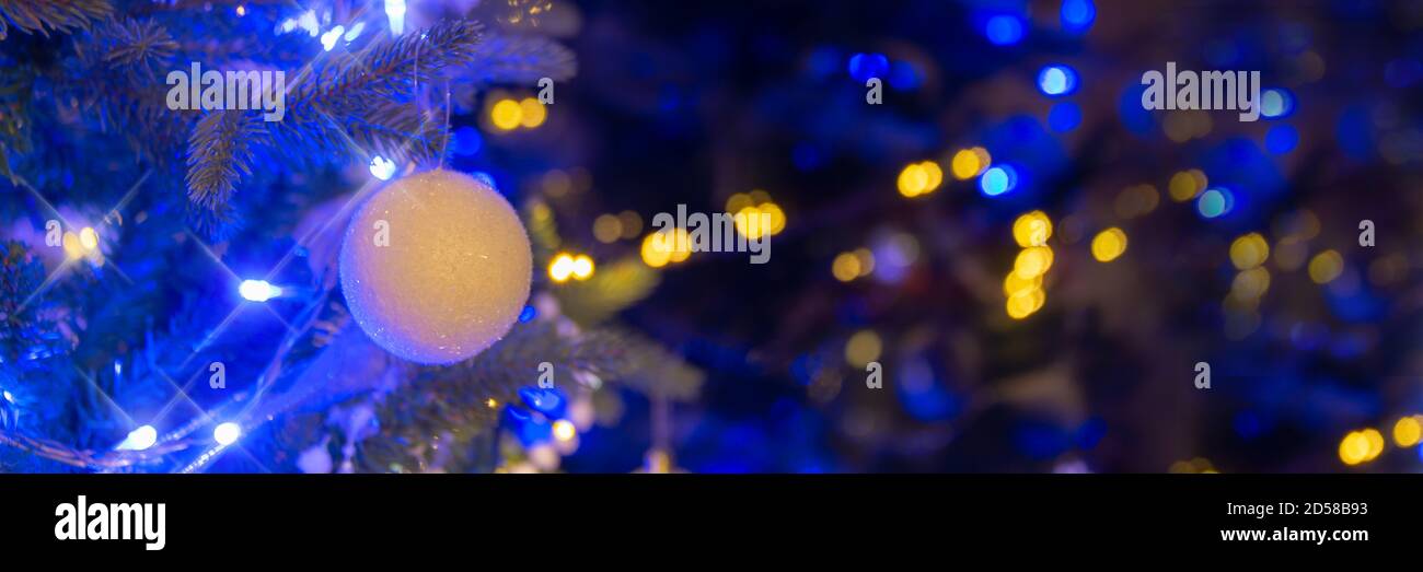 Pallina bianca appesa su un albero di Natale, ornamenti di Natale di notte, blu e oro luci di vacanza sfondo panoramico Foto Stock