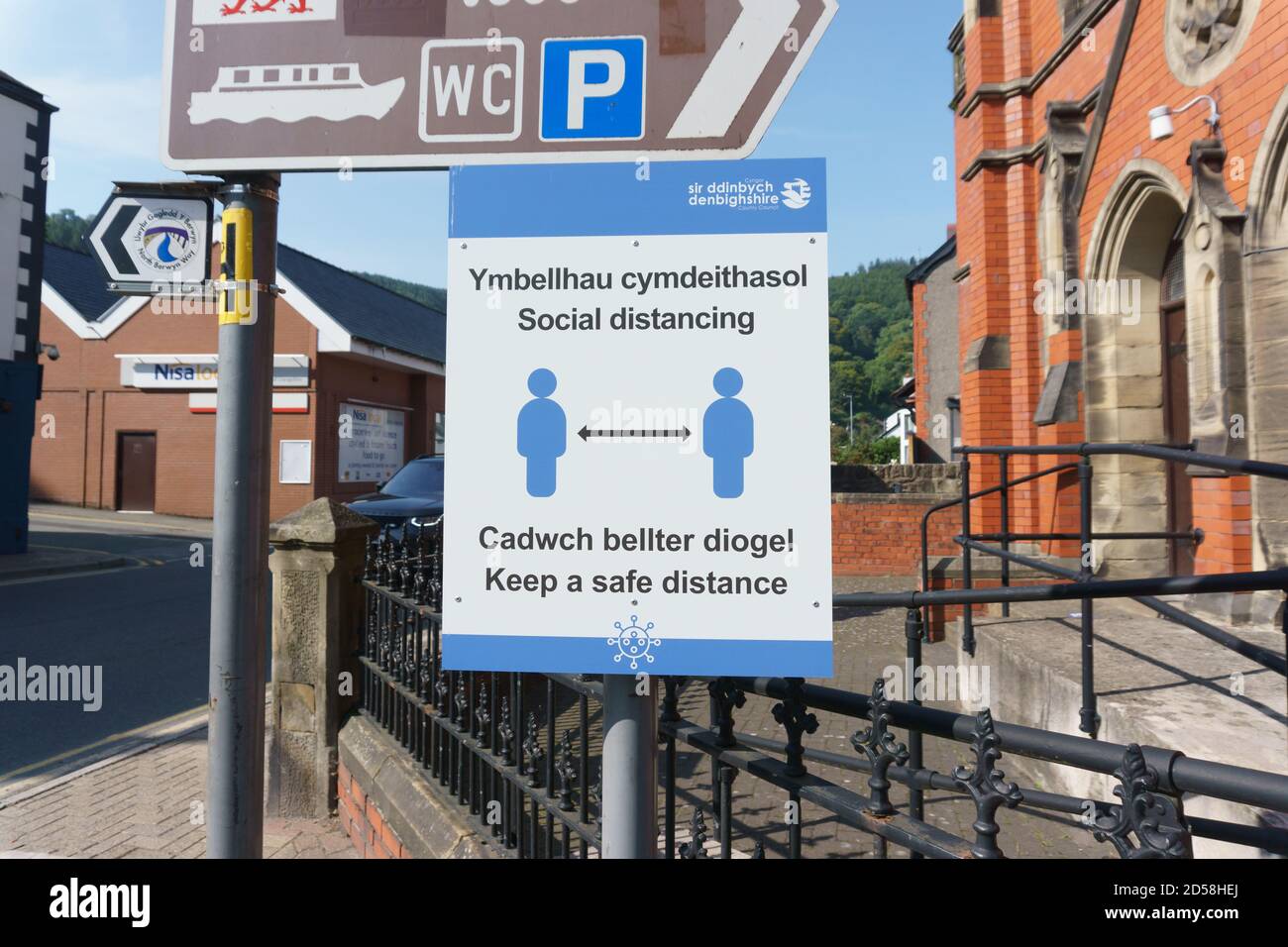 Avviso di allontanamento sociale su una strada pubblica in inglese e. Lingua gallese che dice alle persone di mantenere una distanza sicura durante La pandemia di Coronavirus Foto Stock