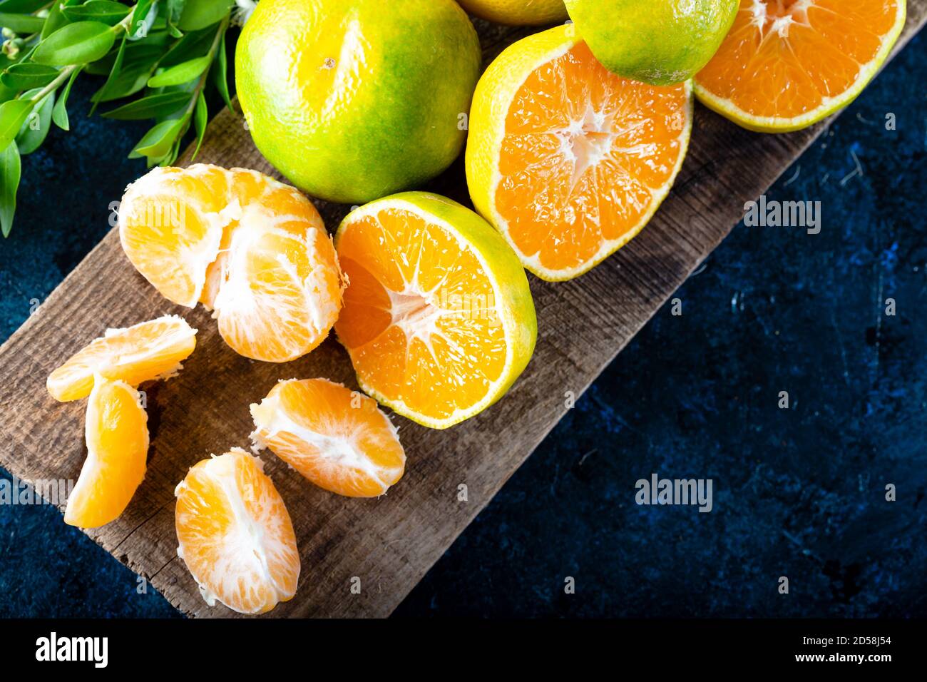 Frutta Mandarina matura sbucciata aperta e posto su vecchio legno rustico aspetto con gruppo di frutta e foglie di mandarino. Frutta invernale. Foto Stock