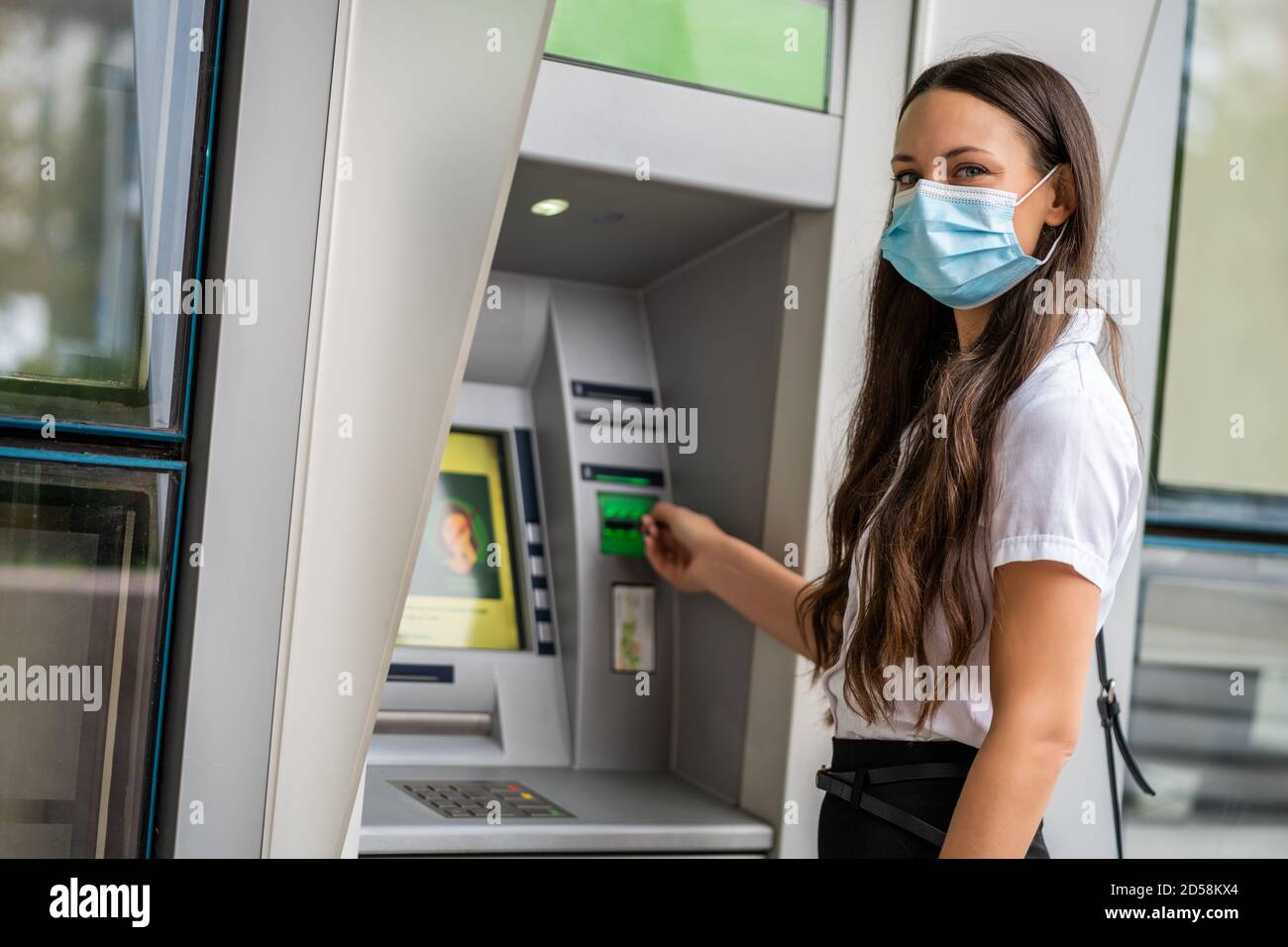Donna d'affari con maschera protettiva sta usando la macchina del bancomat per prelevare i contanti. Concetto di pandemia del virus Covid-19. Foto Stock