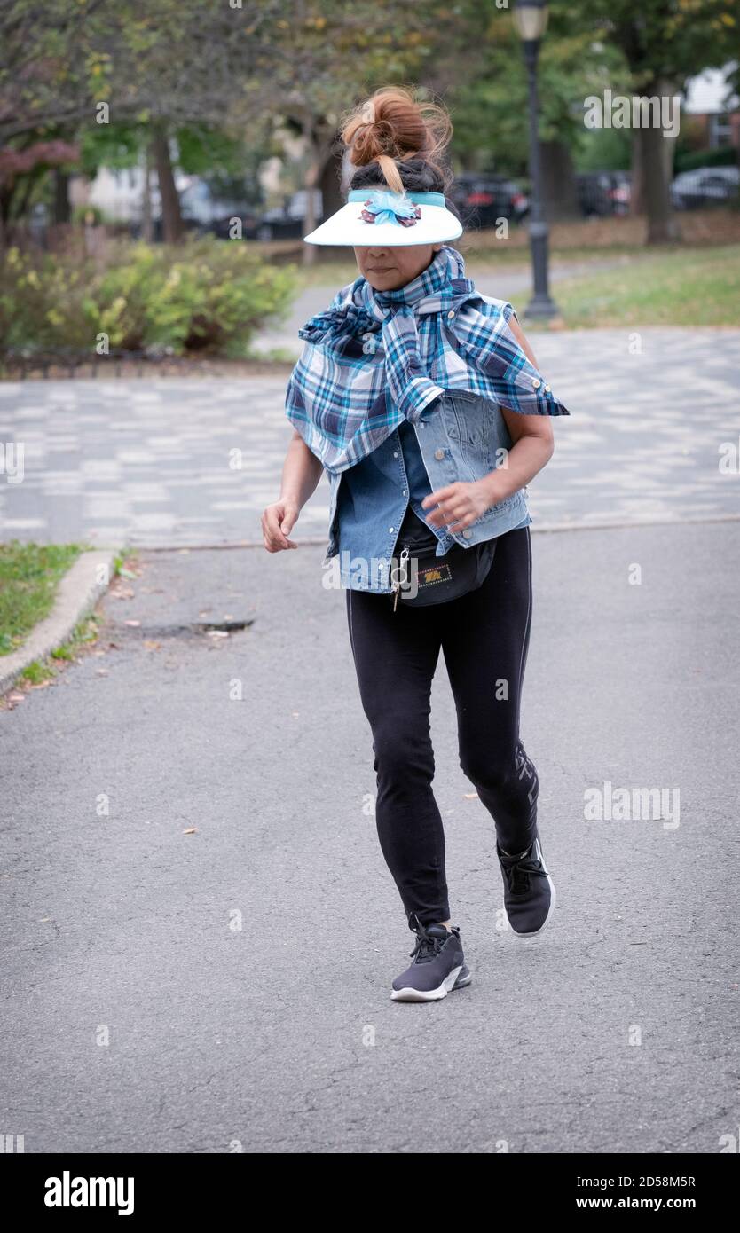 Una foto di una donna asiatica americana con i capelli grandi e un cappello parasole che fa jogging in un parco a Flushing, Queens, New York City. Foto Stock