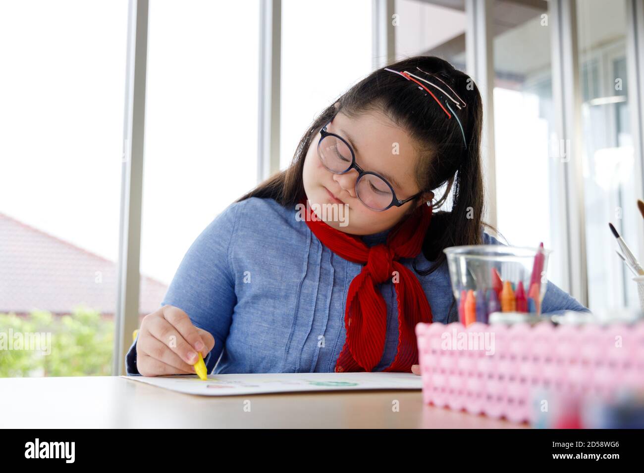 Ragazza con sindrome di Down immagine di disegno con pastello in classe d'arte. Concetto di apprendimento per bambini disabili. Foto Stock