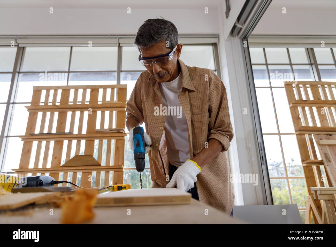 L'uomo anziano asiatico usa il trapano elettrico su tavola di legno in officina di Falegnameria. Concetto di persone anziane che fanno hobby dopo il pensionamento. Foto Stock