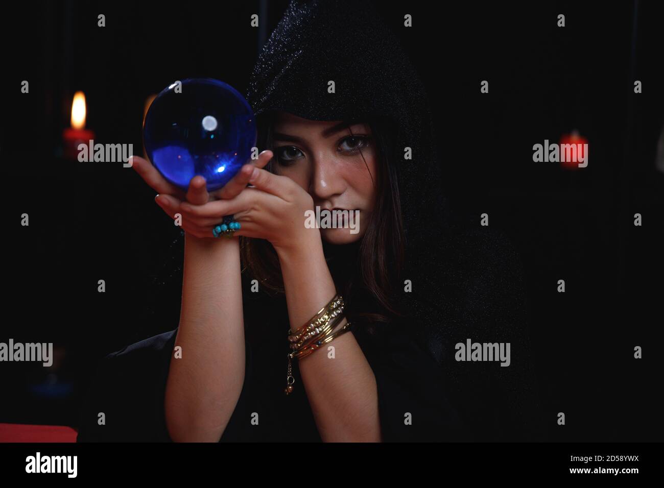 Ritratto di cassiere di fortuna asiatica nel cappuccio nero che tiene la sfera di cristallo blu. Foto Stock