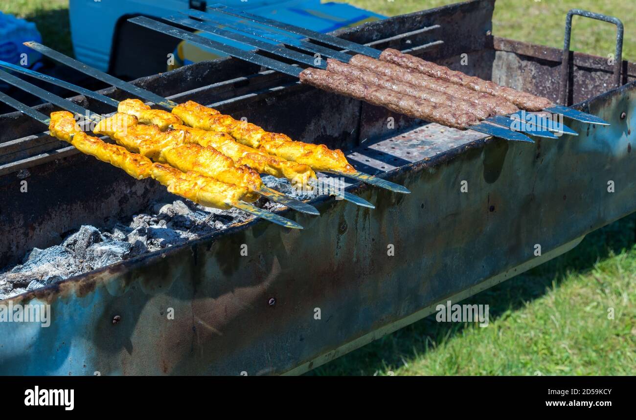Kabobs mediorientale su un barbecue. Ci sono sia kabobs di pollo gialli che kabobs di manzo marrone. Sono inclinati con coltelli metallici piatti sopra un lungo Foto Stock