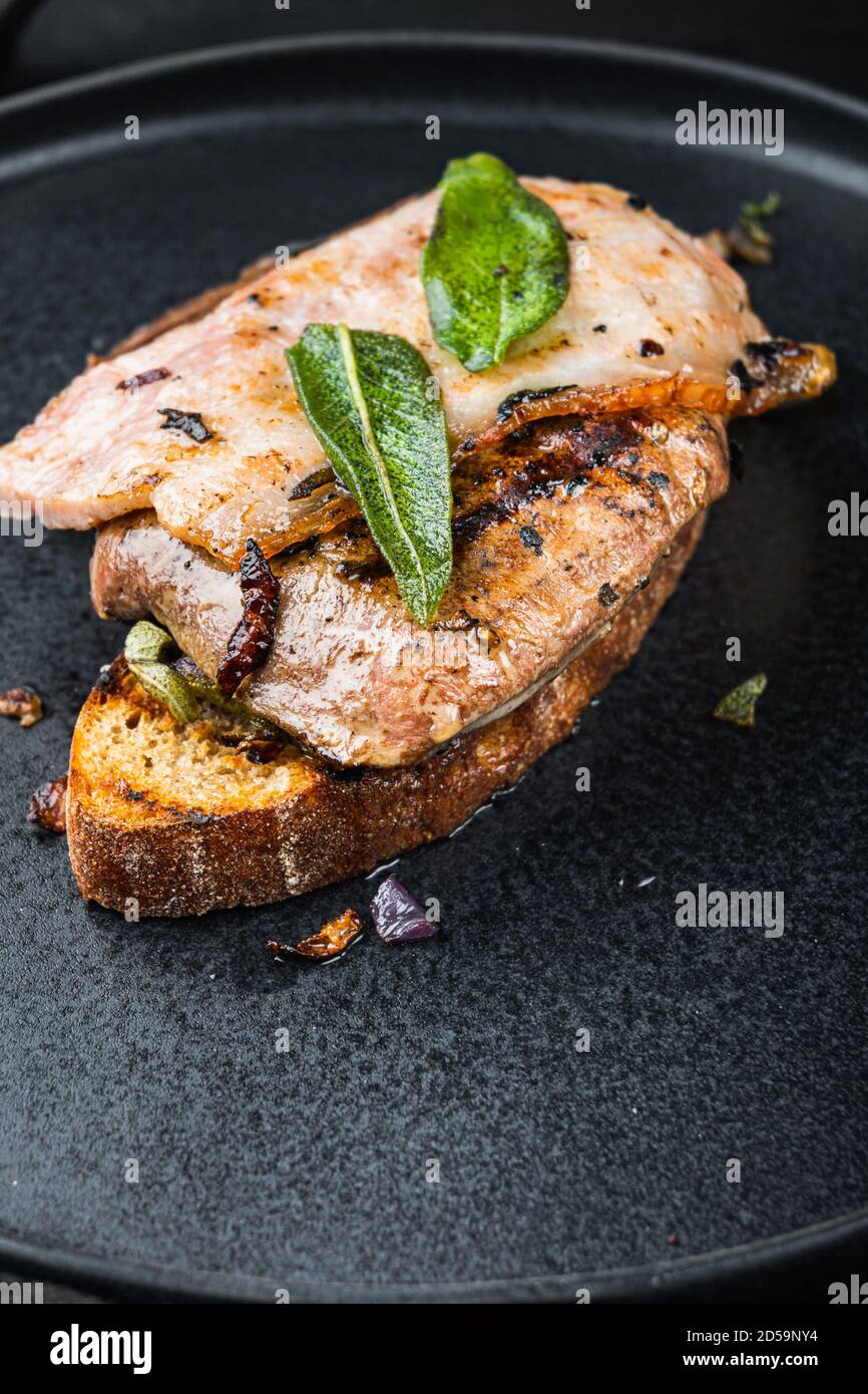 Pancetta di fegato e cipolle sul pane cotto pasto sul piatto su superficie nera Foto Stock