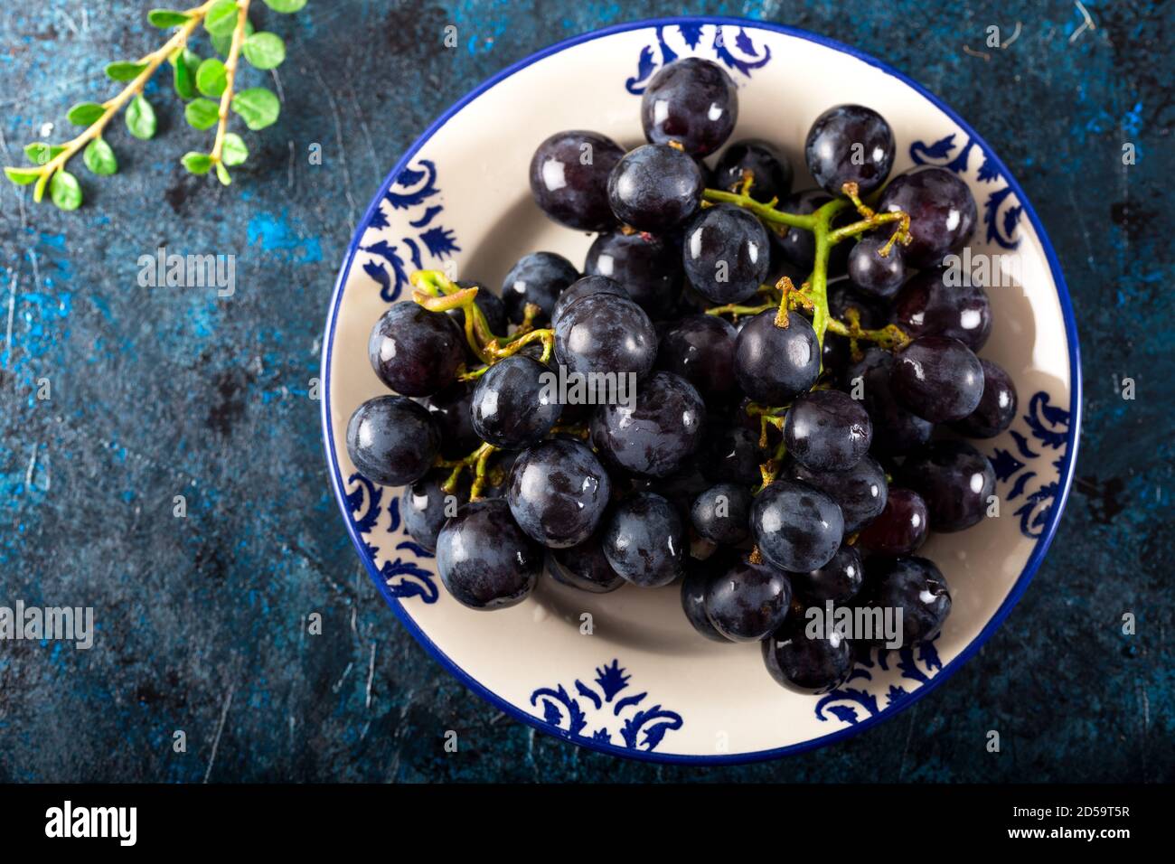 Uve nere fresche e foglie in piatto su sfondo scuro. Foto Stock