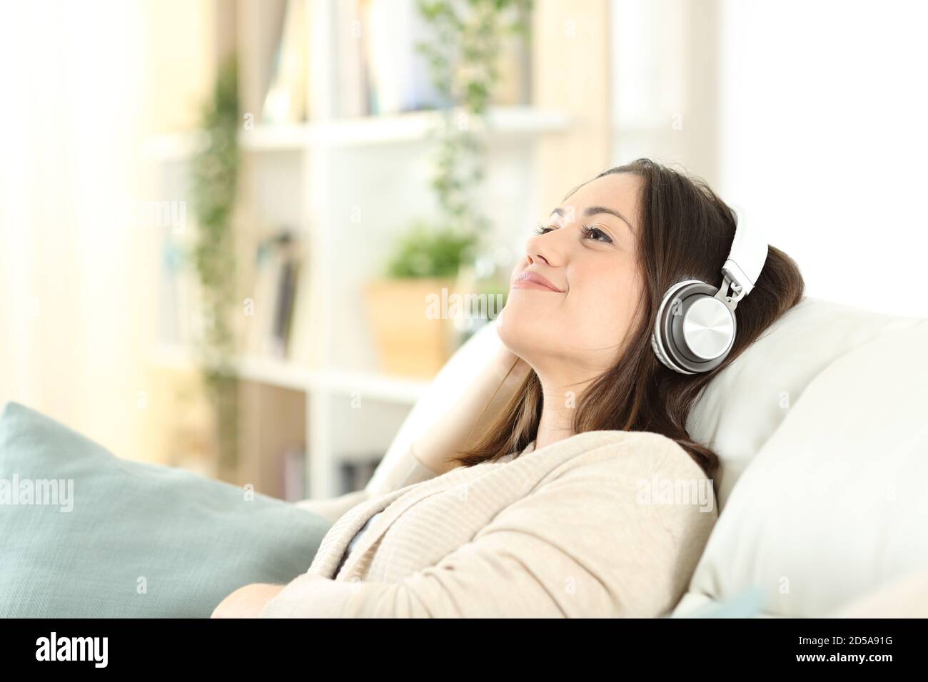 Donna soddisfatta che si rilassa seduto su un divano ascoltando musica a casa Foto Stock
