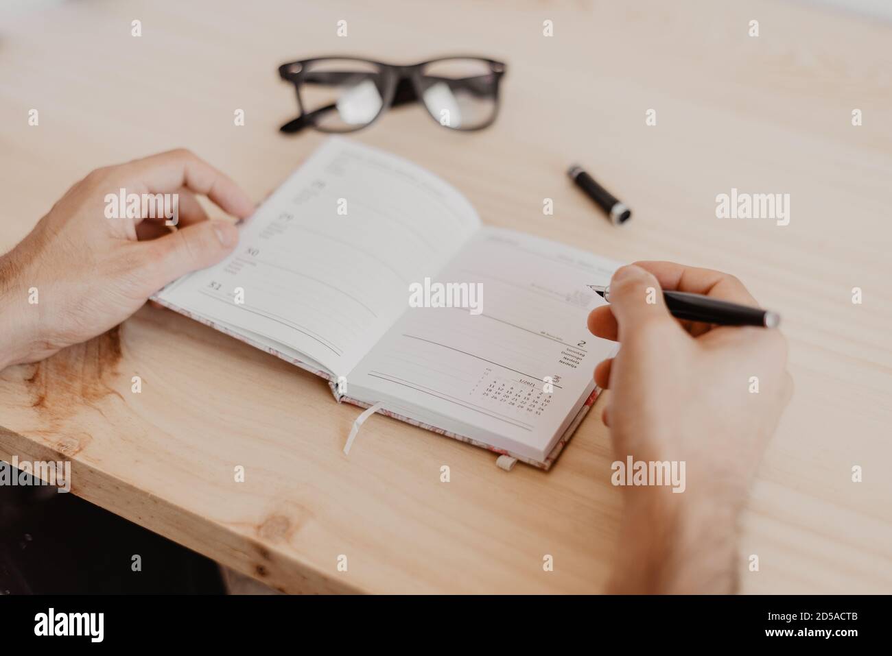 un uomo seduto a una scrivania progetta l'anno 2021 su un diario aperto con una penna in mano e gli occhiali al suo fianco Foto Stock