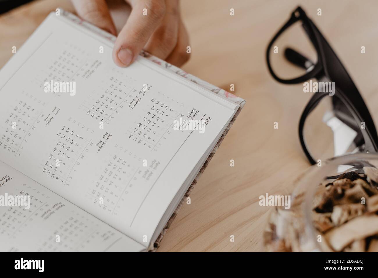 un uomo seduto a una scrivania progetta l'anno 2021 su un diario aperto con gli occhiali al suo fianco Foto Stock