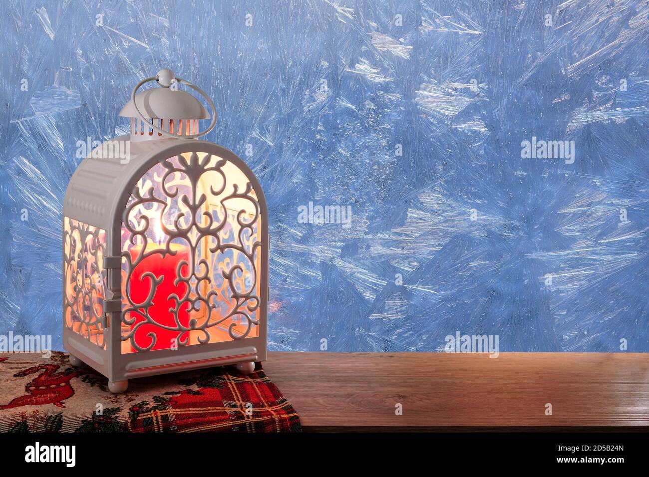 Candela alla finestra congelata. Vetro con motivi di neve. Lampada con una candela alla finestra invernale. Natale e Capodanno. Foto Stock