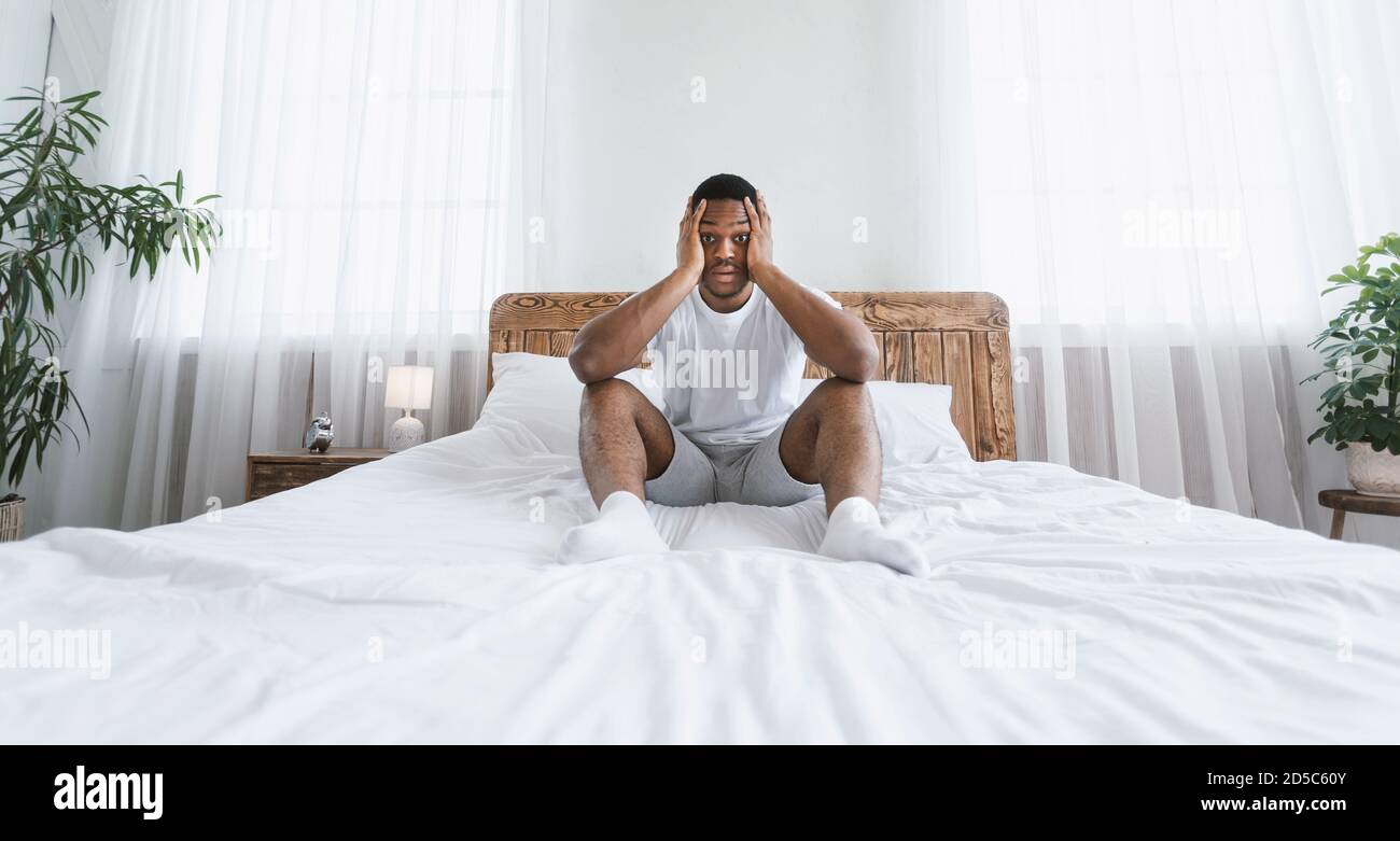 Stressato overslept African American Man seduto a letto a casa Foto Stock
