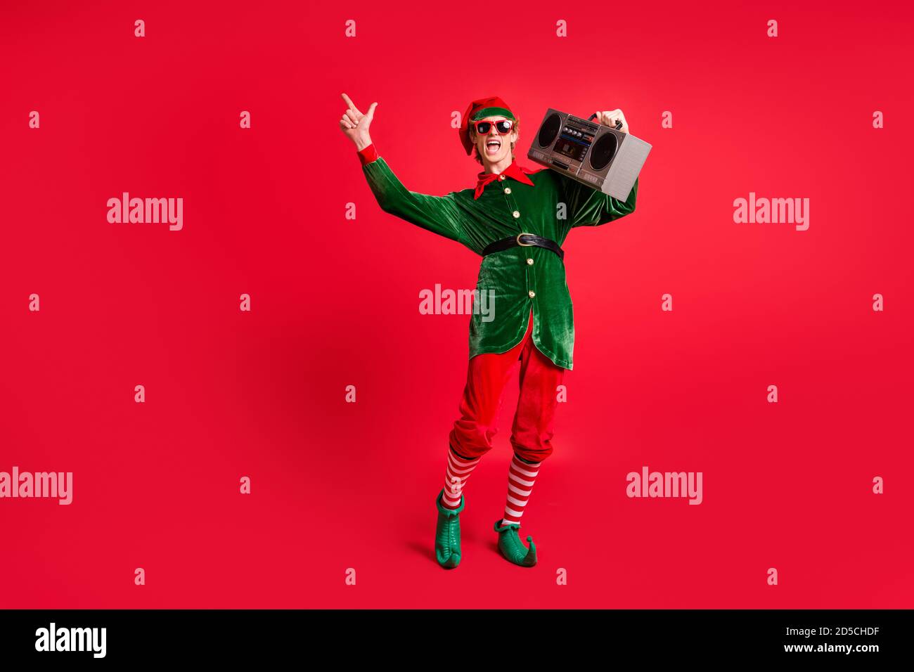 Foto a dimensione intera di pazzo elfo tenere braccio box ascoltare canzoni x-mas isolate su sfondo rosso brillante Foto Stock