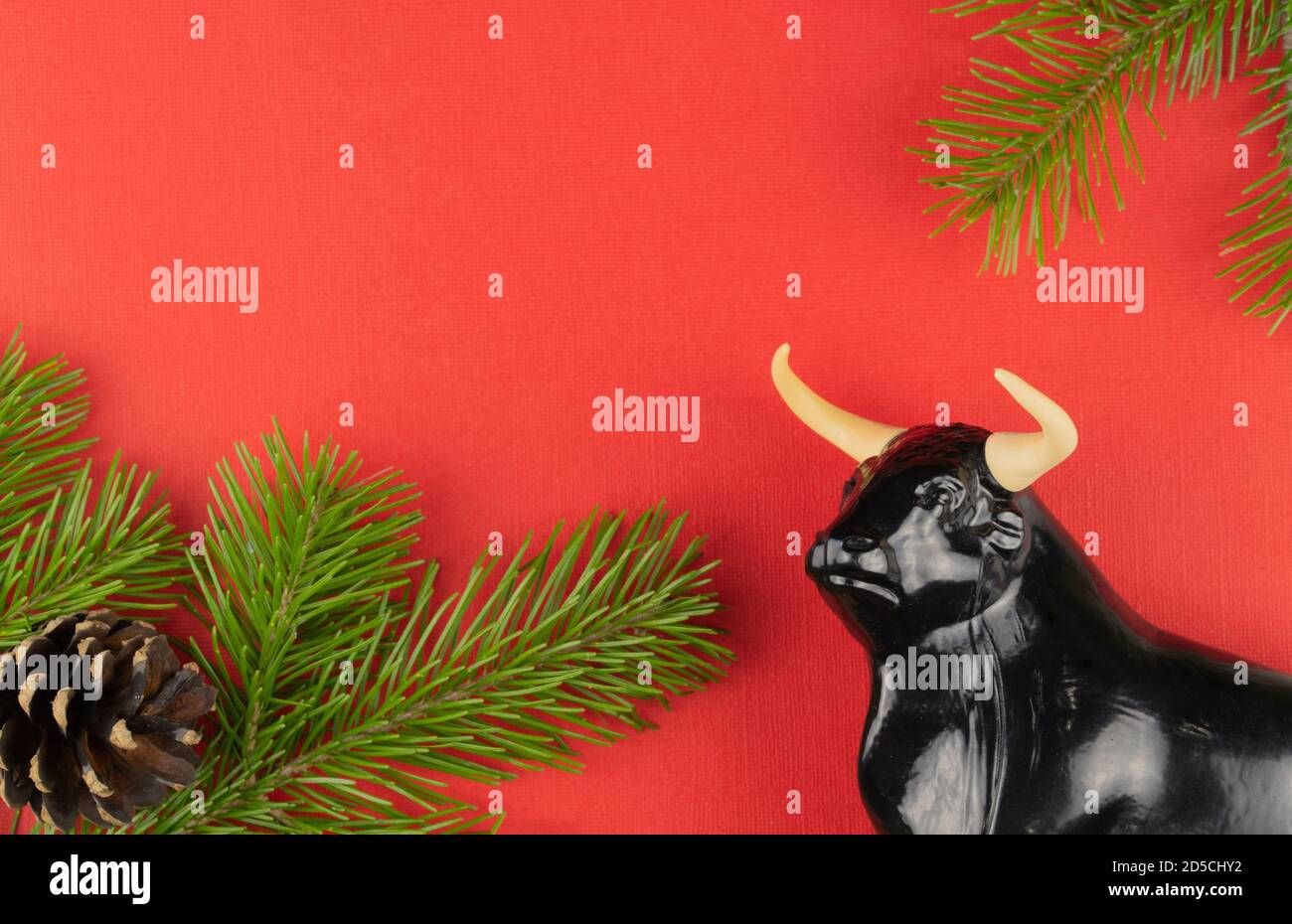 Statuetta di un toro su sfondo rosso Natale. Fuoco selettivo. Decorazioni festive e rami di abete con coni. Foto Stock