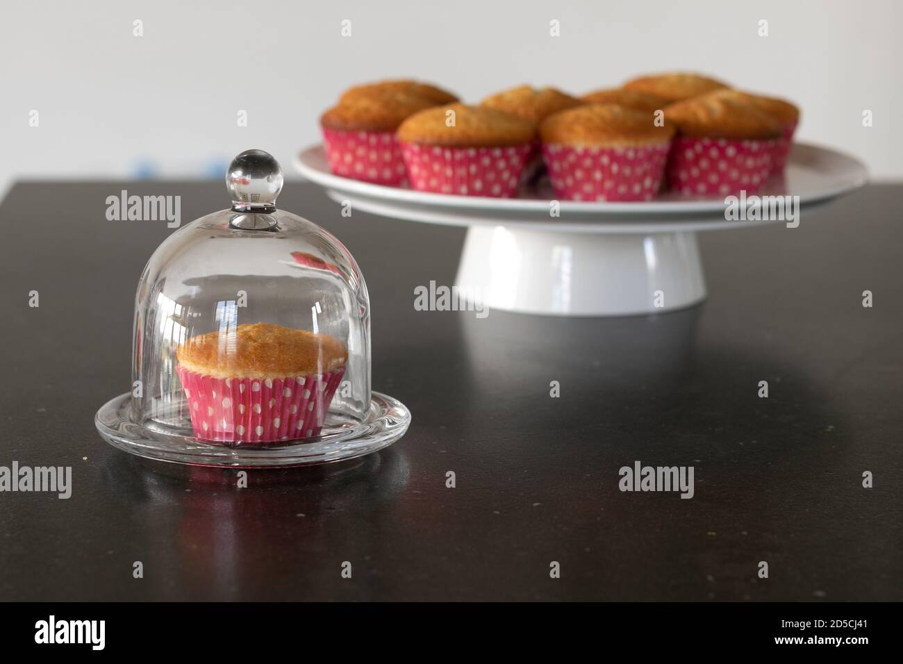 Cupcakes cotto in casa in un piatto bianco o in un vetro e in uno sfondo scuro del tavolo, tazze rosa con i punti del withe, cupcakes semplici senza decorazione. Casa Foto Stock