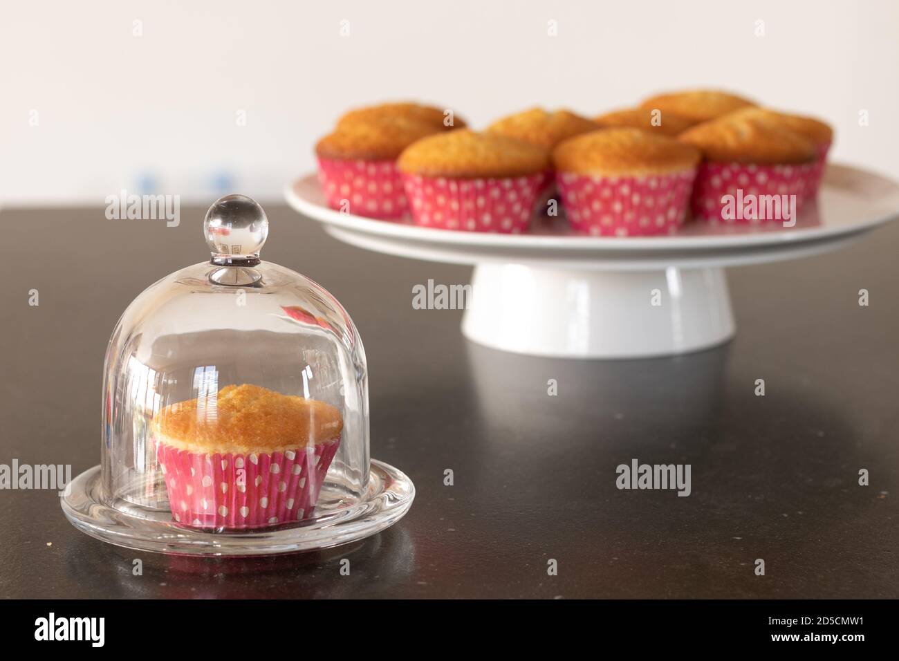 Cupcakes cotto in casa in un piatto bianco o in un vetro e in uno sfondo scuro del tavolo, tazze rosa con i punti del withe, cupcakes semplici senza decorazione. Casa Foto Stock
