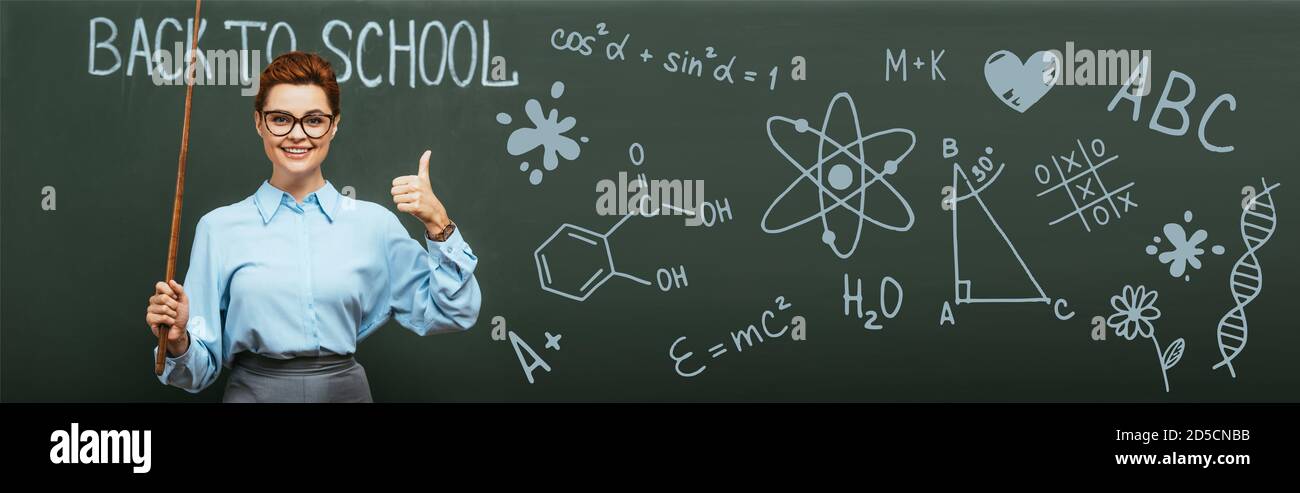 panoramica di insegnante di chimica con bastone di puntamento che mostra il pollice vicino alla lavagna con scritte e illustrazioni di ritorno a scuola Foto Stock