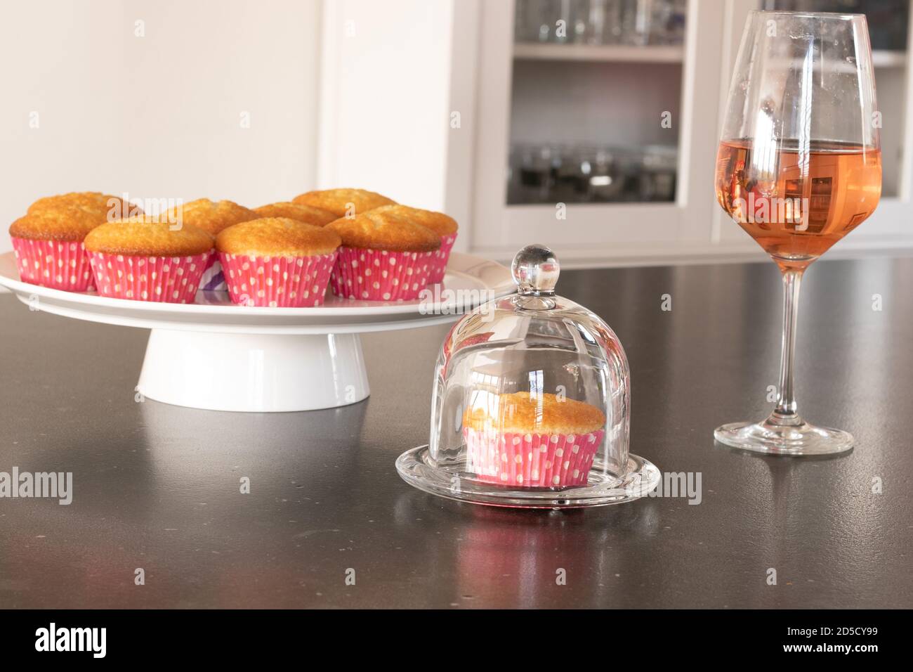 Cupcakes cotto in casa in un piatto bianco o in un vetro e in uno sfondo scuro del tavolo, tazze rosa con i punti del withe, cupcakes semplici senza decorazione. Casa Foto Stock
