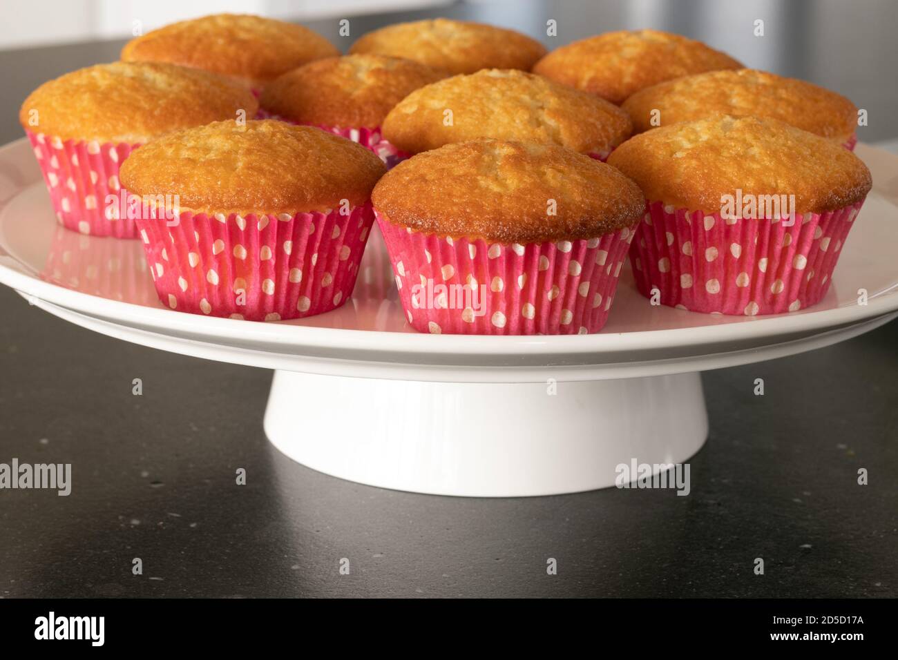 Cupcakes cotto in casa in un piatto bianco o in un vetro e in uno sfondo scuro del tavolo, tazze rosa con i punti del withe, cupcakes semplici senza decorazione. Casa Foto Stock
