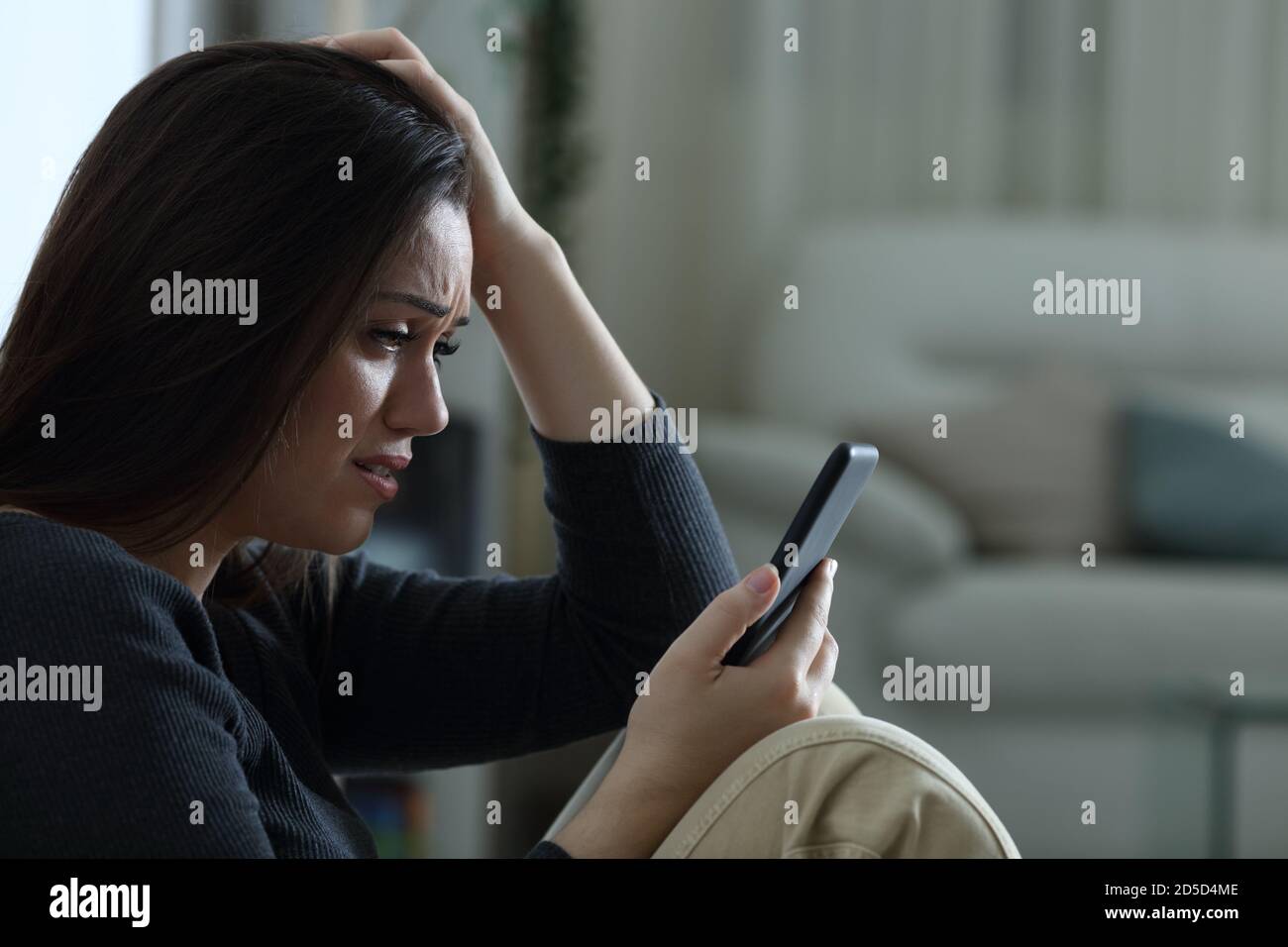 Donna triste che legge le notizie difettose sul telefono mobile che si lamenta a. casa di notte Foto Stock