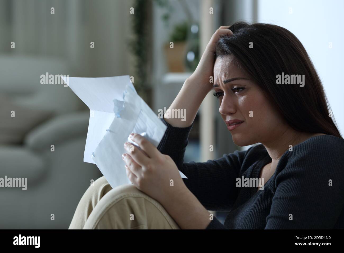 Donna triste che legge una lettera che si lamenta da sola a casa in la notte Foto Stock