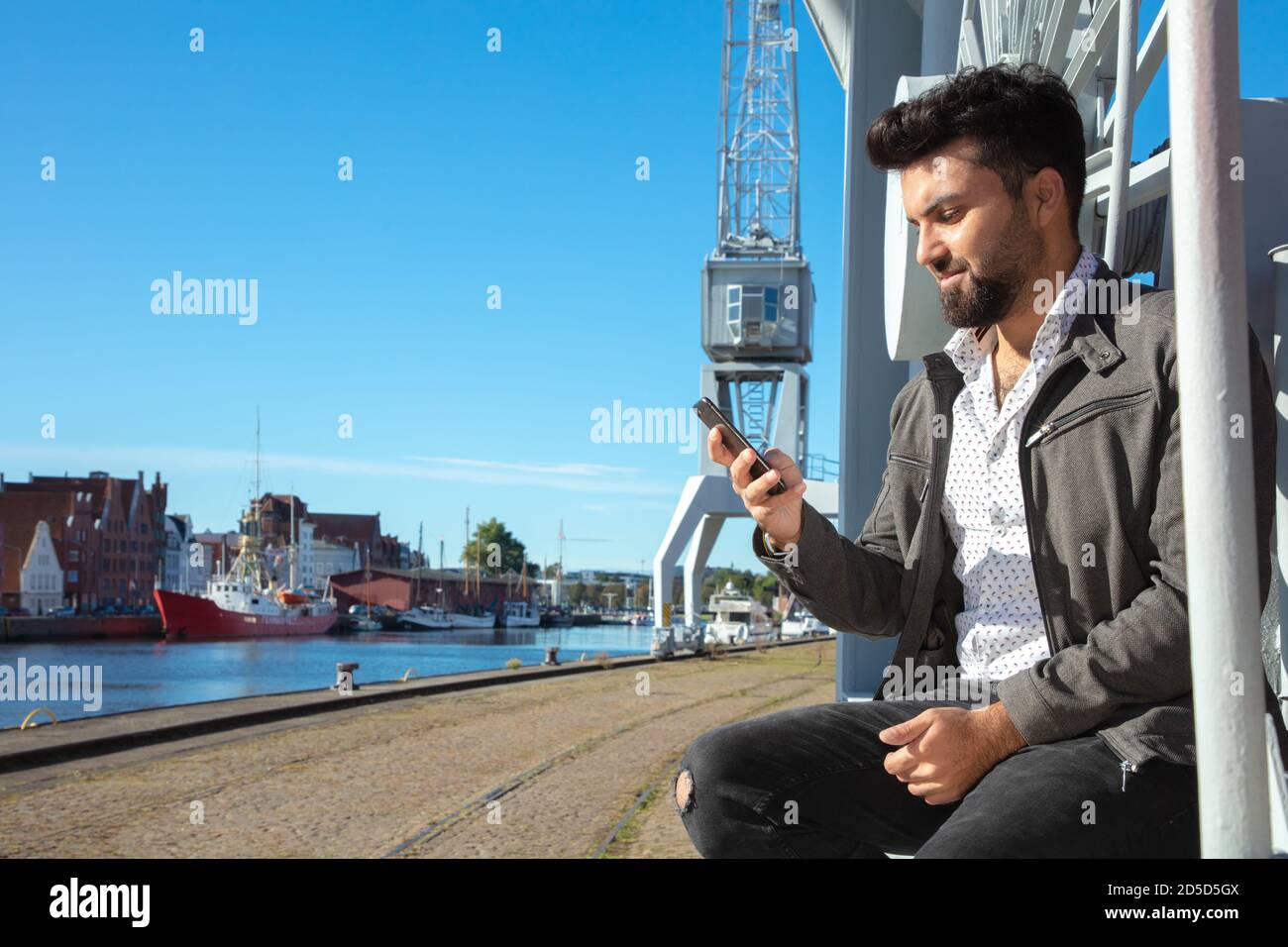 Mann steht fröhlich am Hafen, smartphone in der hand Foto Stock