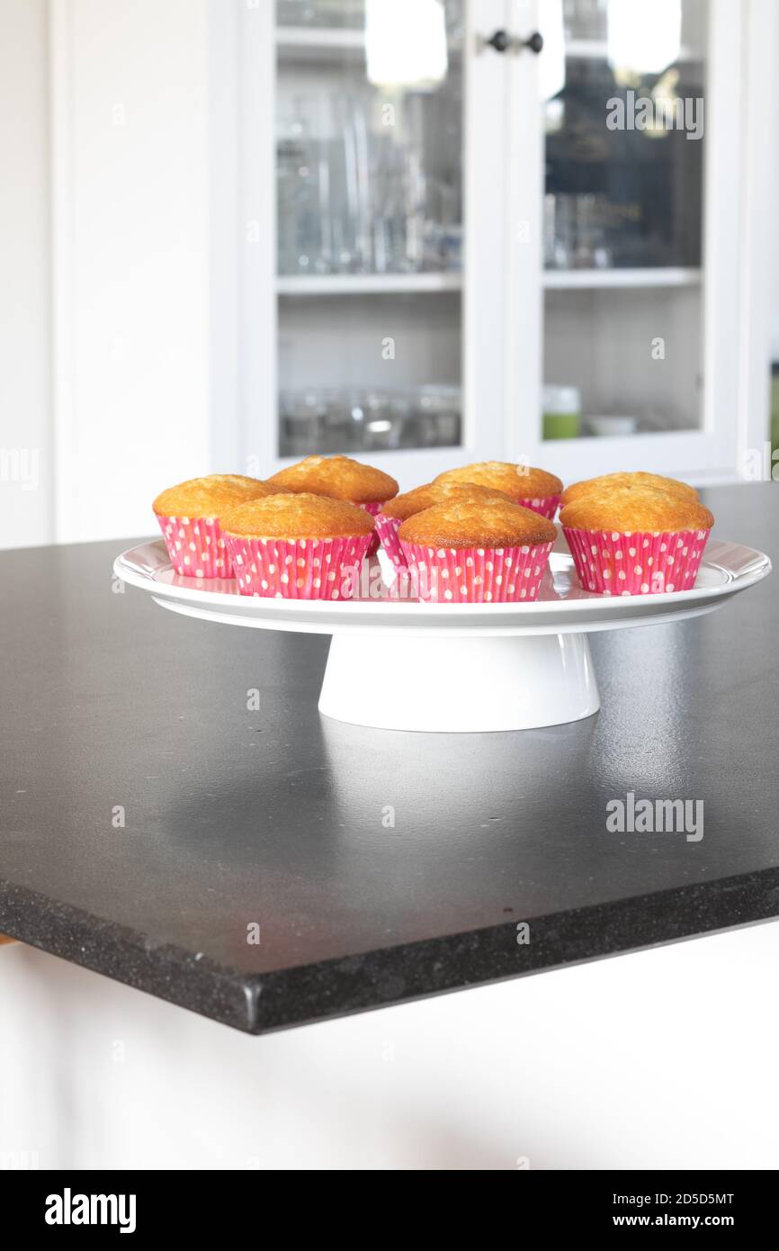 Cupcakes cotto in casa in un piatto bianco o in un vetro e in uno sfondo scuro del tavolo, tazze rosa con i punti del withe, cupcakes semplici senza decorazione. Casa Foto Stock
