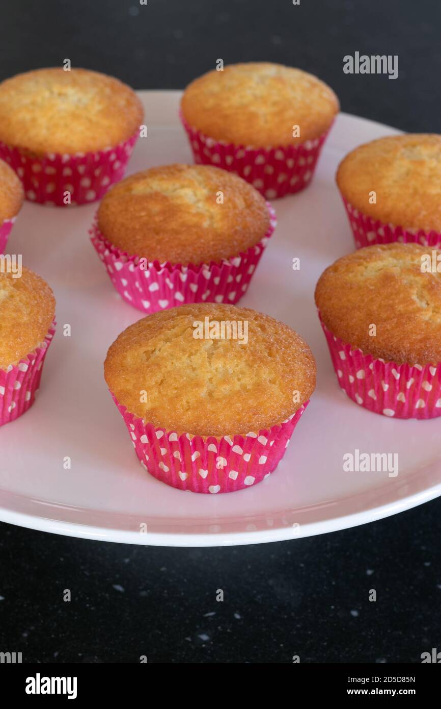 Cupcakes cotto in casa in un piatto bianco o in un vetro e in uno sfondo scuro del tavolo, tazze rosa con i punti del withe, cupcakes semplici senza decorazione. Casa Foto Stock