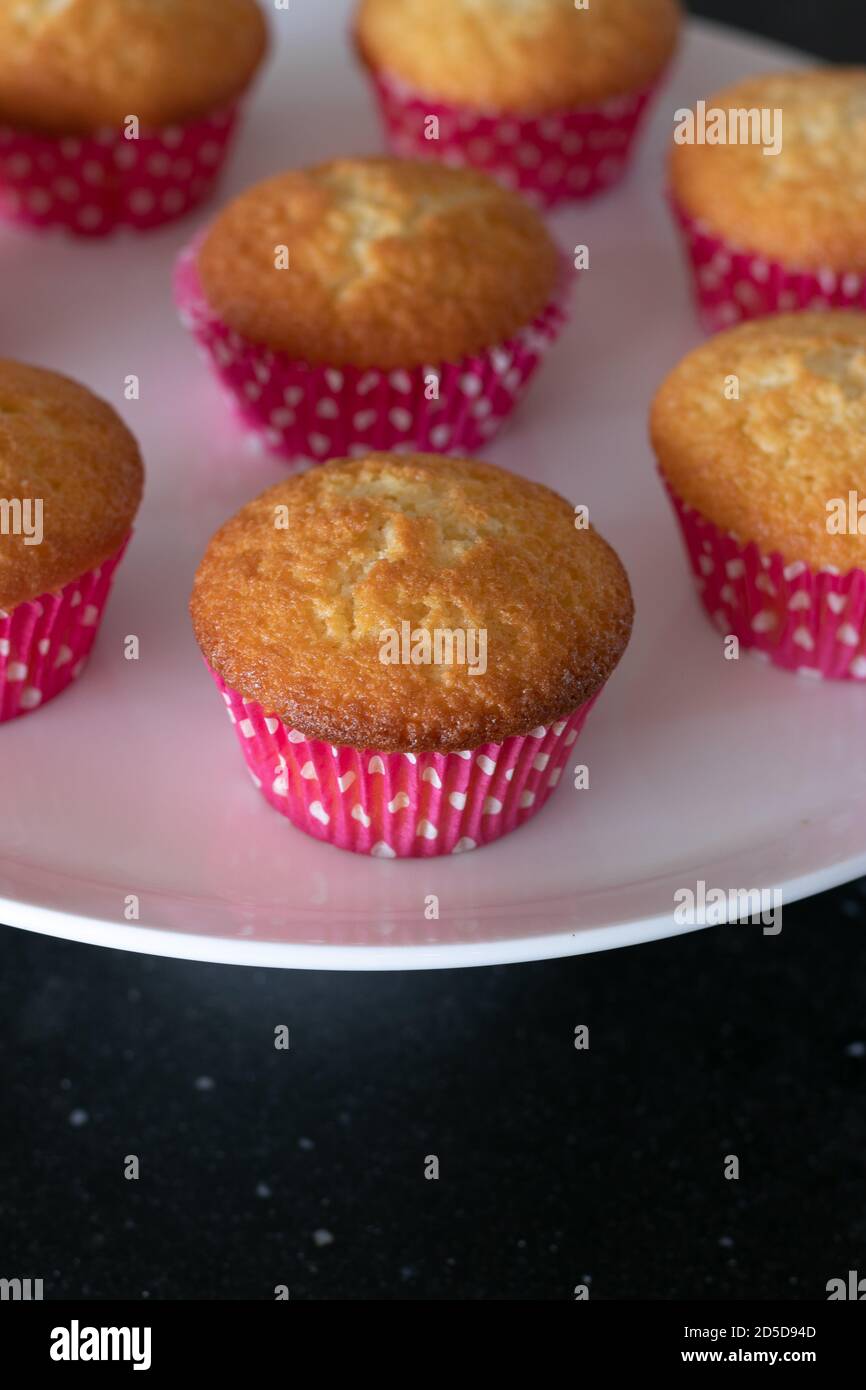 Cupcakes cotto in casa in un piatto bianco o in un vetro e in uno sfondo scuro del tavolo, tazze rosa con i punti del withe, cupcakes semplici senza decorazione. Casa Foto Stock