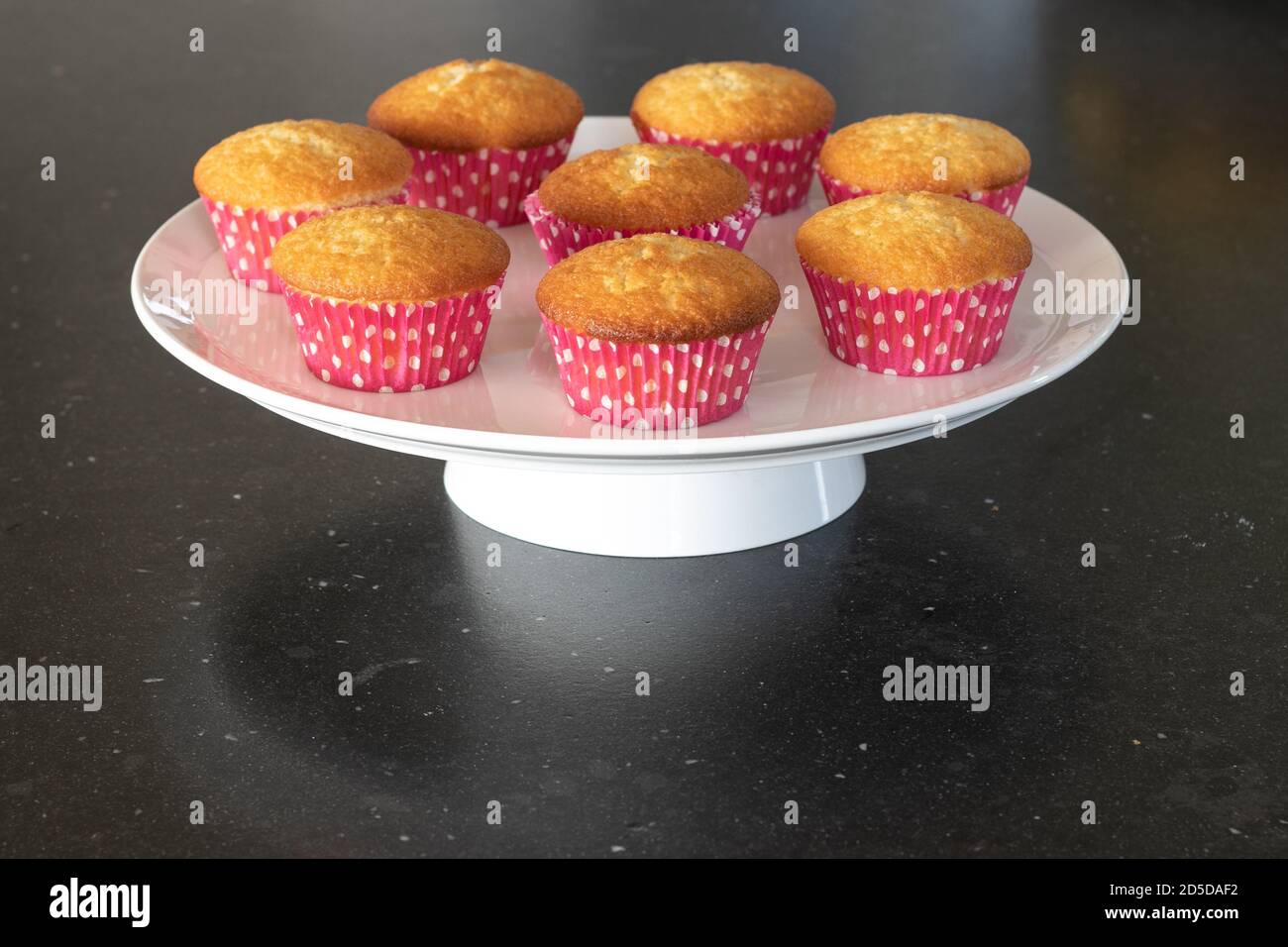 Cupcakes cotto in casa in un piatto bianco o in un vetro e in uno sfondo scuro del tavolo, tazze rosa con i punti del withe, cupcakes semplici senza decorazione. Casa Foto Stock