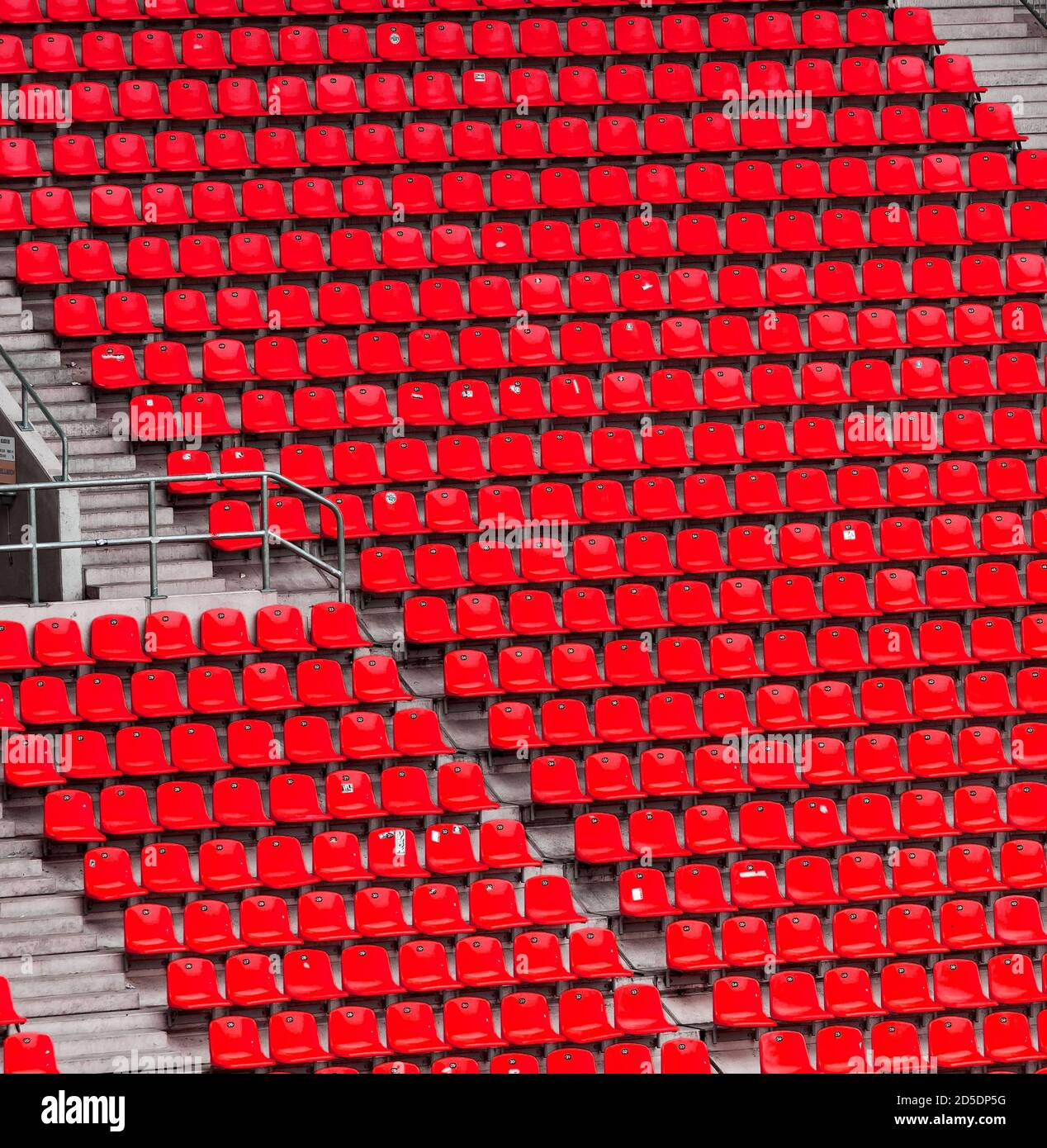 Molte file di posti a sedere rossi in un grande stadio sportivo senza spettatori con scale in cemento. Foto Stock