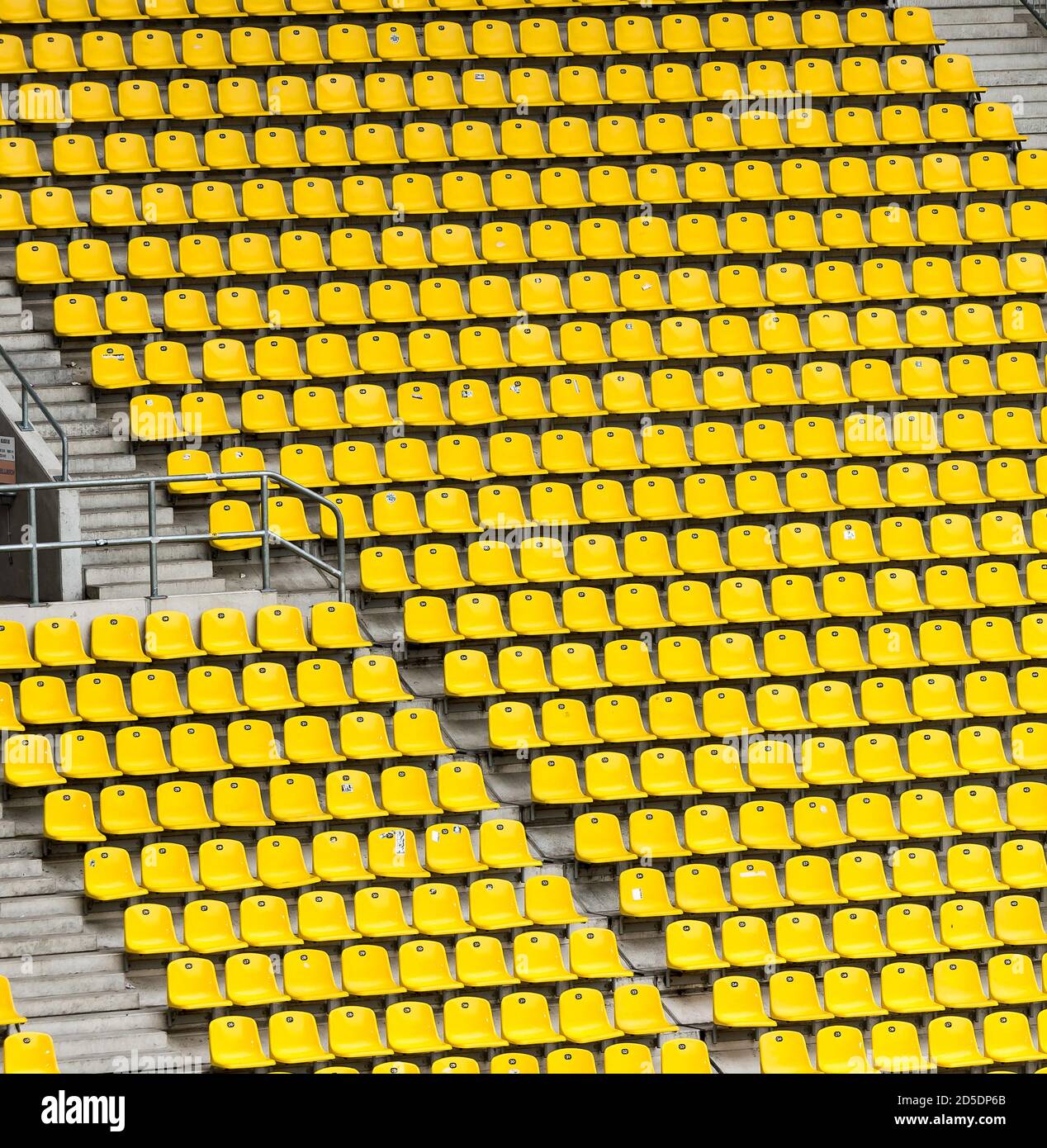 Molte file di posti gialli in un grande stadio sportivo senza spettatori con scale di cemento. Foto Stock