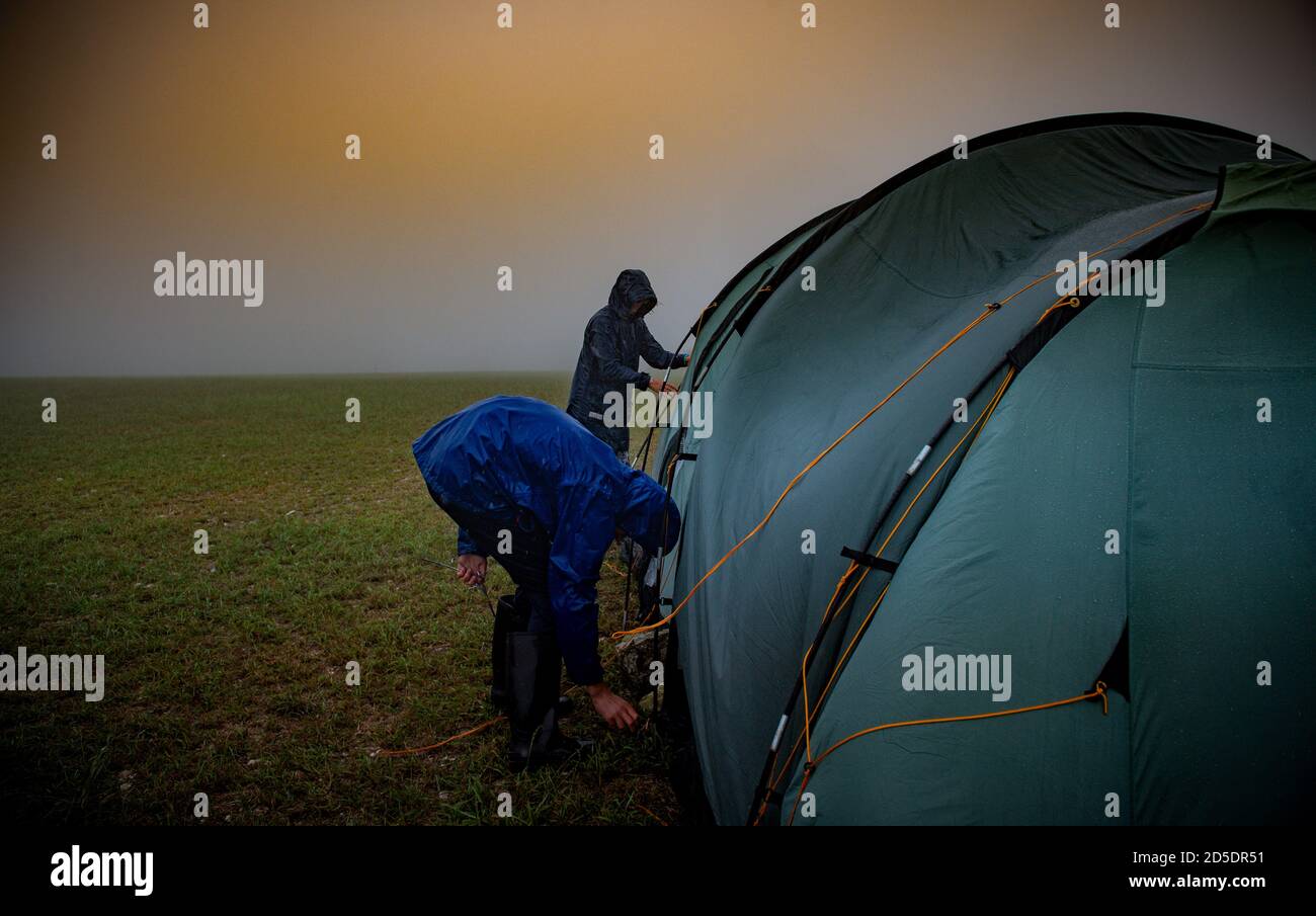 Una madre e un figlio tentano di fissare una tenda in condizioni climatiche estreme con forte vento e pioggia durante una vacanza in campeggio. Foto Stock