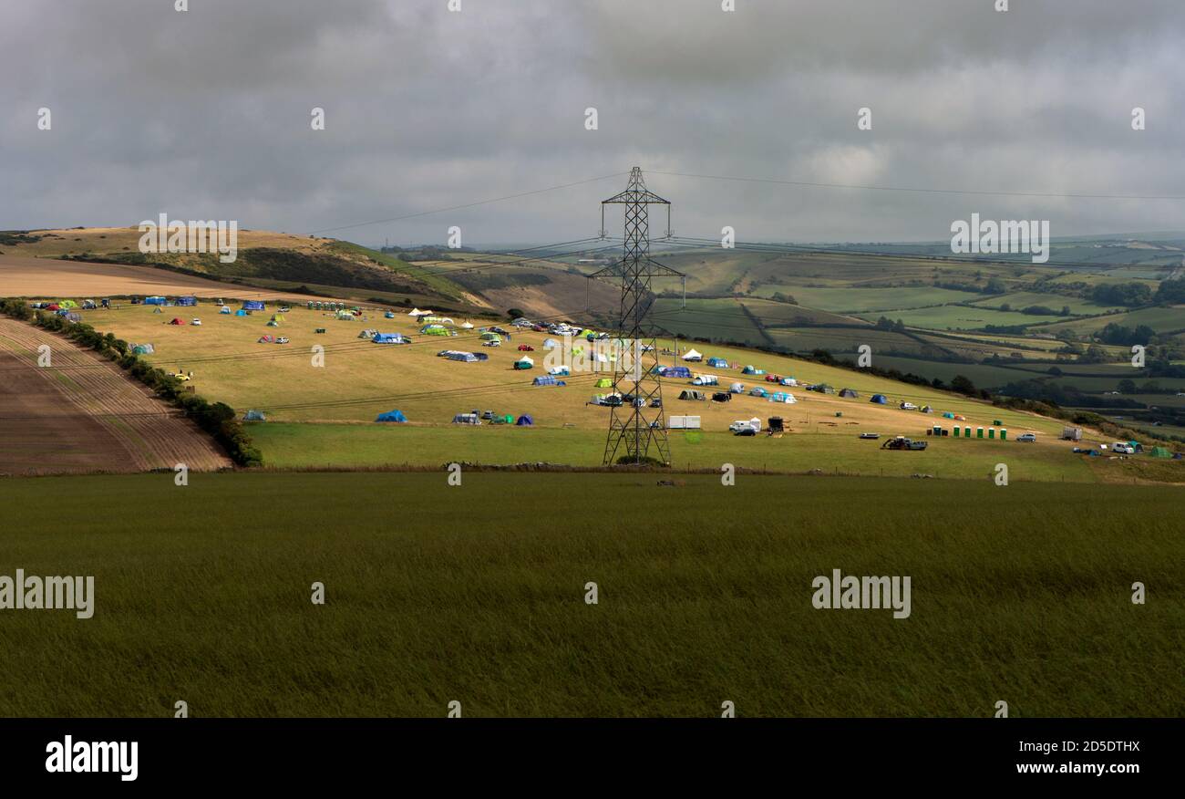 Una vista sulla campagna del Dorset con un campeggio di tende in lontananza e una torre elettrica a reticolo. Foto Stock